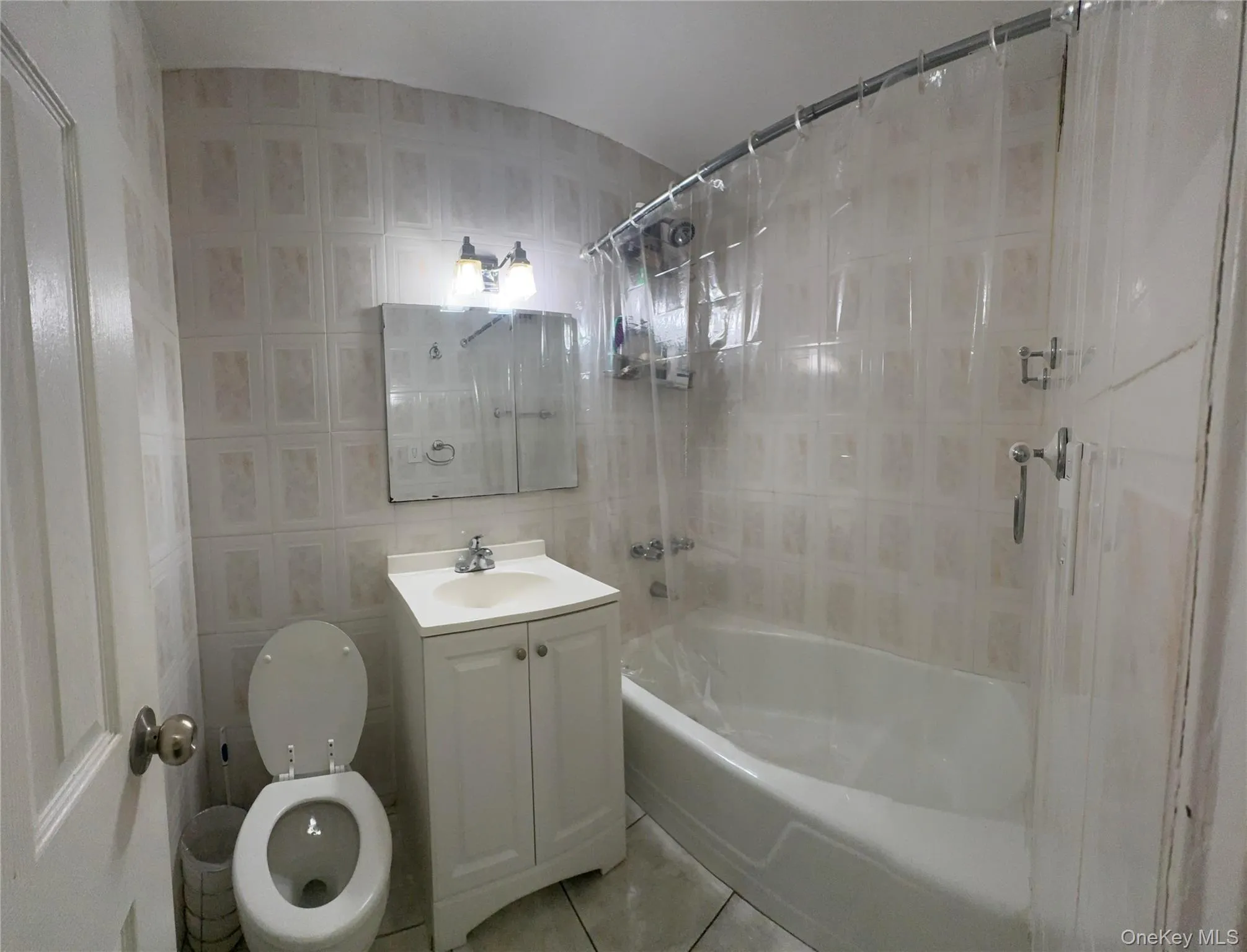 Full bathroom featuring vanity, bathing tub / shower combination, tile walls, and light tile patterned floors Full bathroom featuring vanity, bathing tub / shower combination, tile walls, and light tile patterned floors
