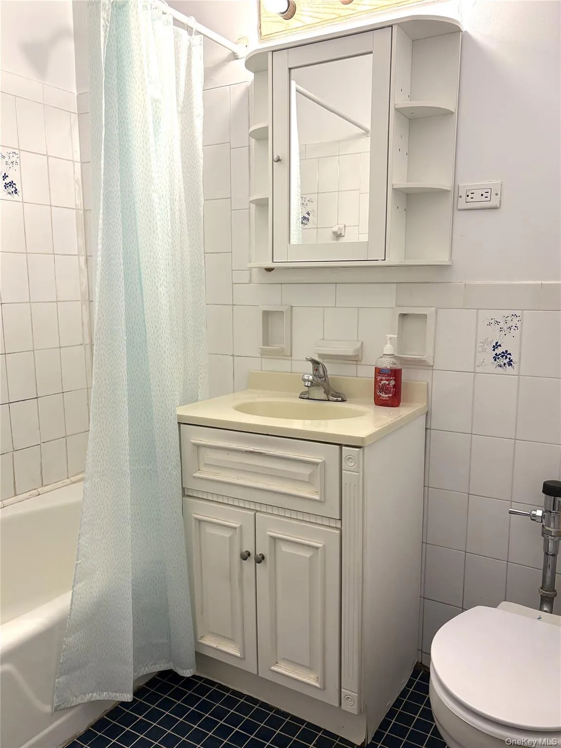 Bathroom featuring tile patterned flooring, toilet, vanity, tile walls, and shower / tub combo with curtain Bathroom featuring tile patterned flooring, toilet, vanity, tile walls, and shower / tub combo with curtain
