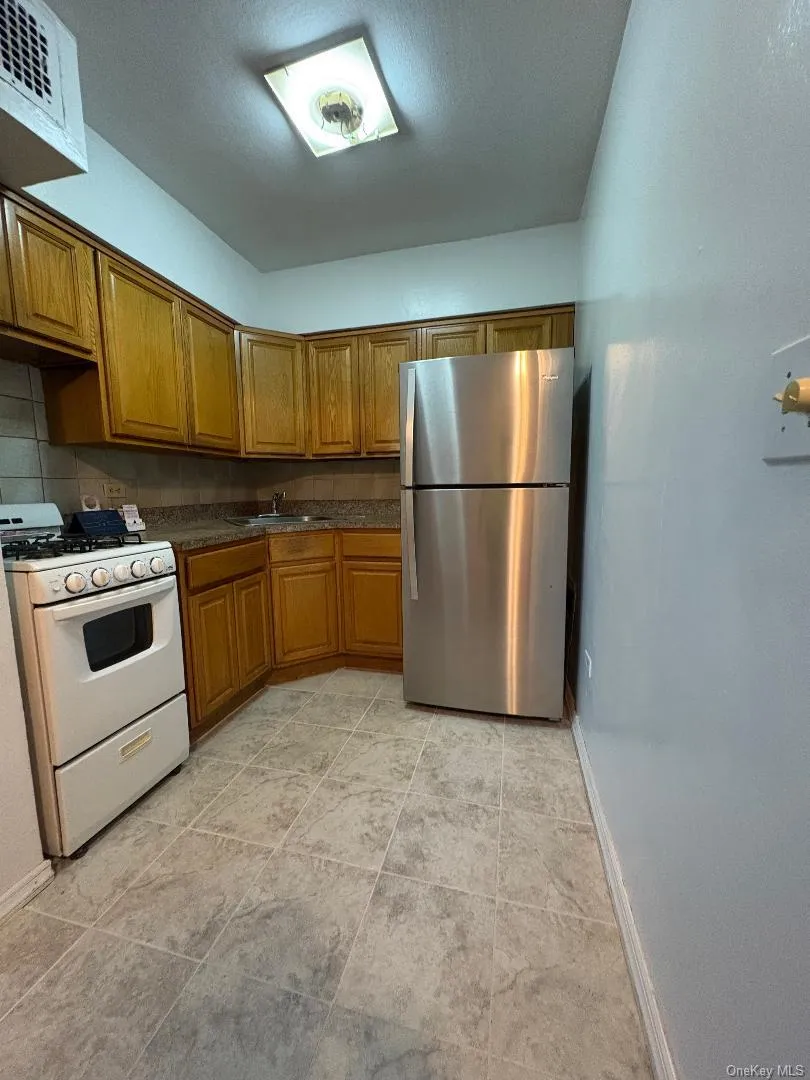 Kitchen featuring brown cabinets, white gas stove, freestanding refrigerator, decorative backsplash, and light tile patterned floors Kitchen featuring brown cabinets, white gas stove, freestanding refrigerator, decorative backsplash, and light tile patterned floors