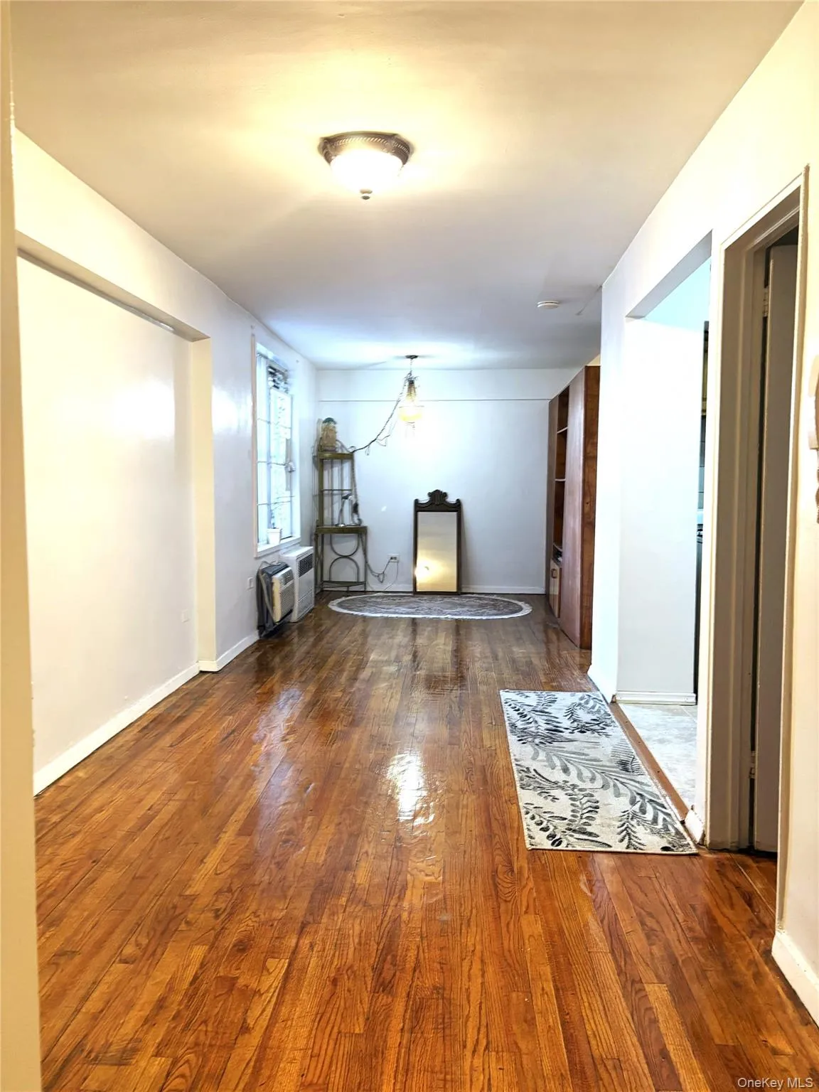 Corridor with wood finished floors, an AC wall unit, and baseboards Corridor with wood finished floors, an AC wall unit, and baseboards