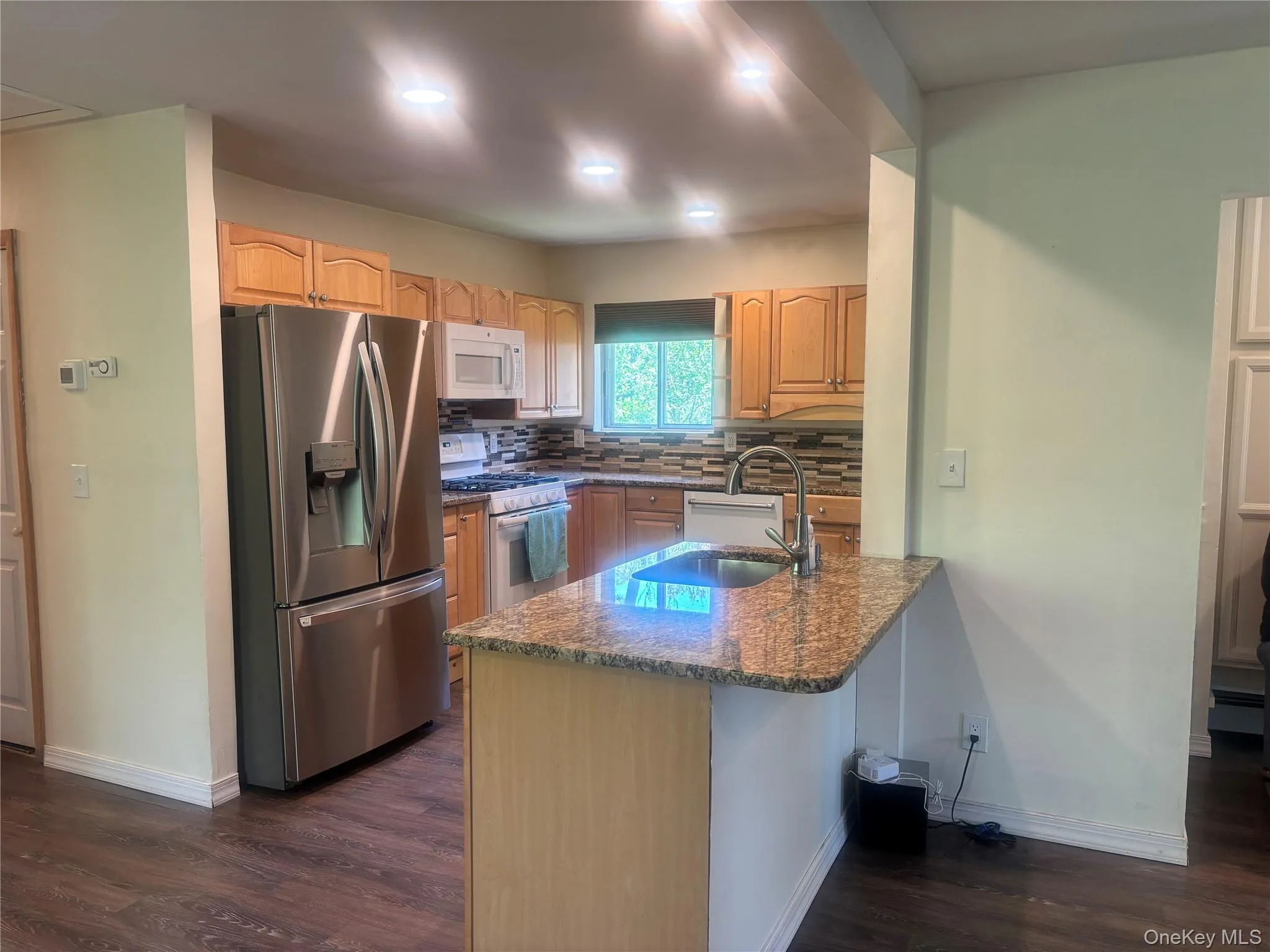 Kitchen with white appliances, dark stone countertops, dark wood-type flooring, a peninsula, and decorative backsplash Kitchen with white appliances, dark stone countertops, dark wood-type flooring, a peninsula, and decorative backsplash