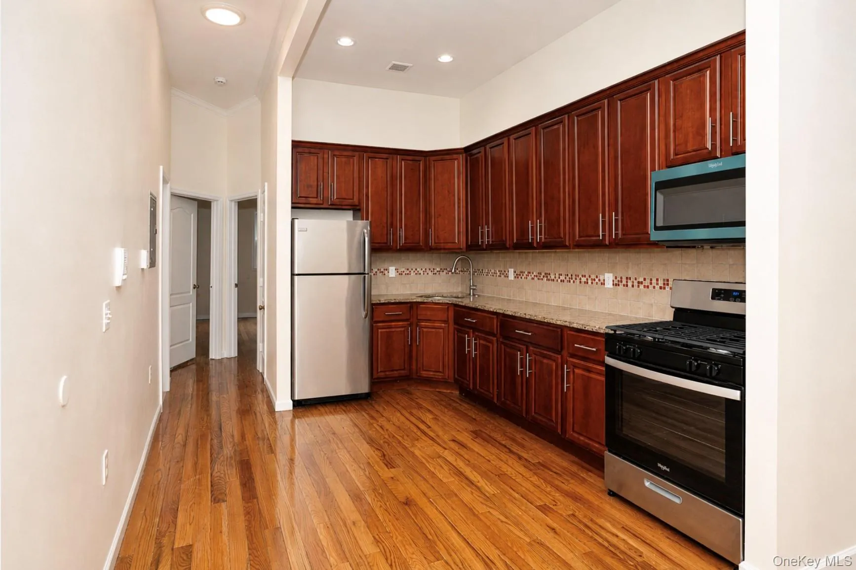 Kitchen featuring dark wood cabinetry, stainless steel appliances, light-toned countertops, and a patterned tile backsplash. Kitchen featuring dark wood cabinetry, stainless steel appliances, light-toned countertops, and a patterned tile backsplash.