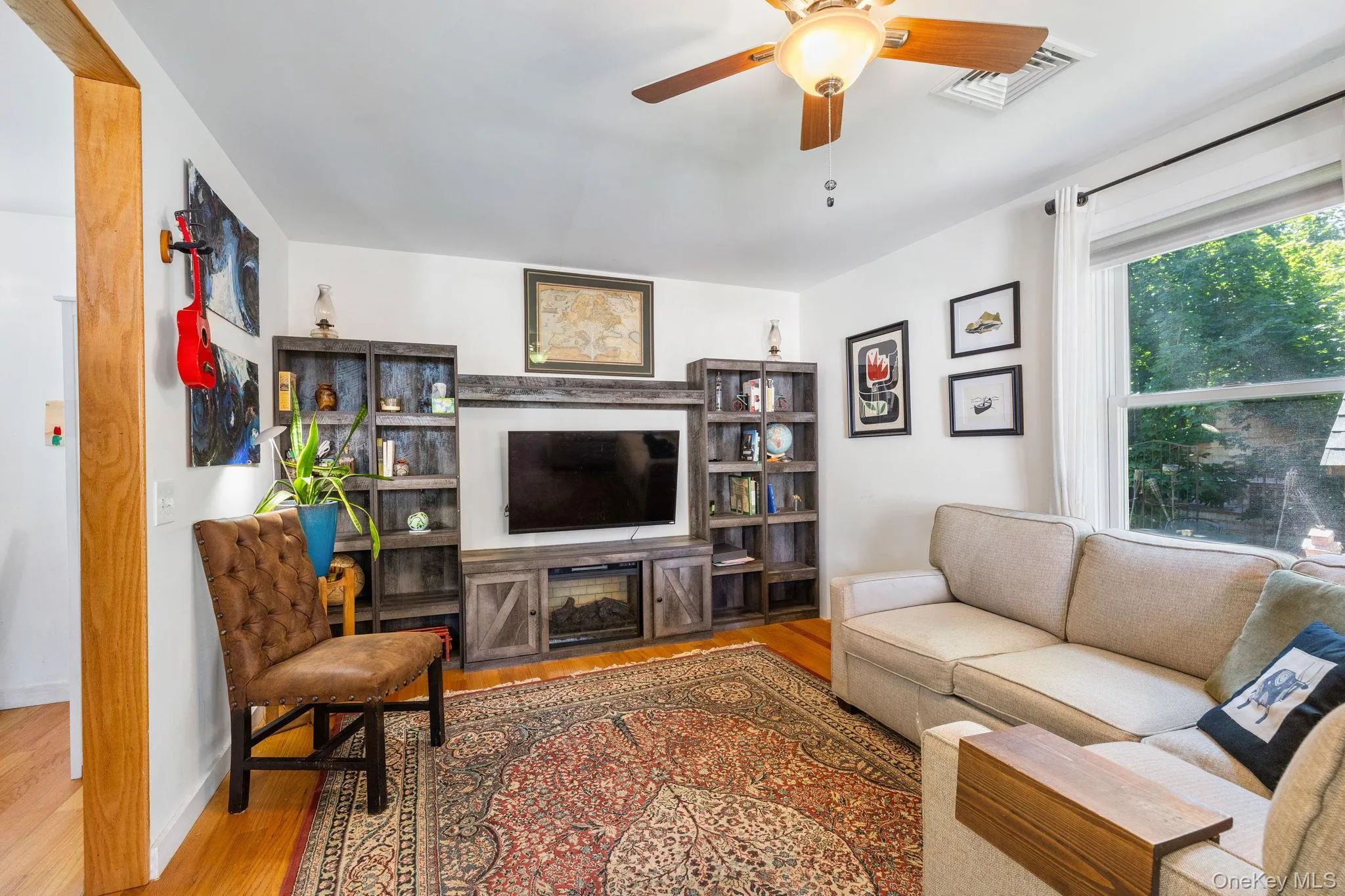 Hardwood flooring, entertainment center, ceiling fan with integrated lighting, and a large window Hardwood flooring, entertainment center, ceiling fan with integrated lighting, and a large window