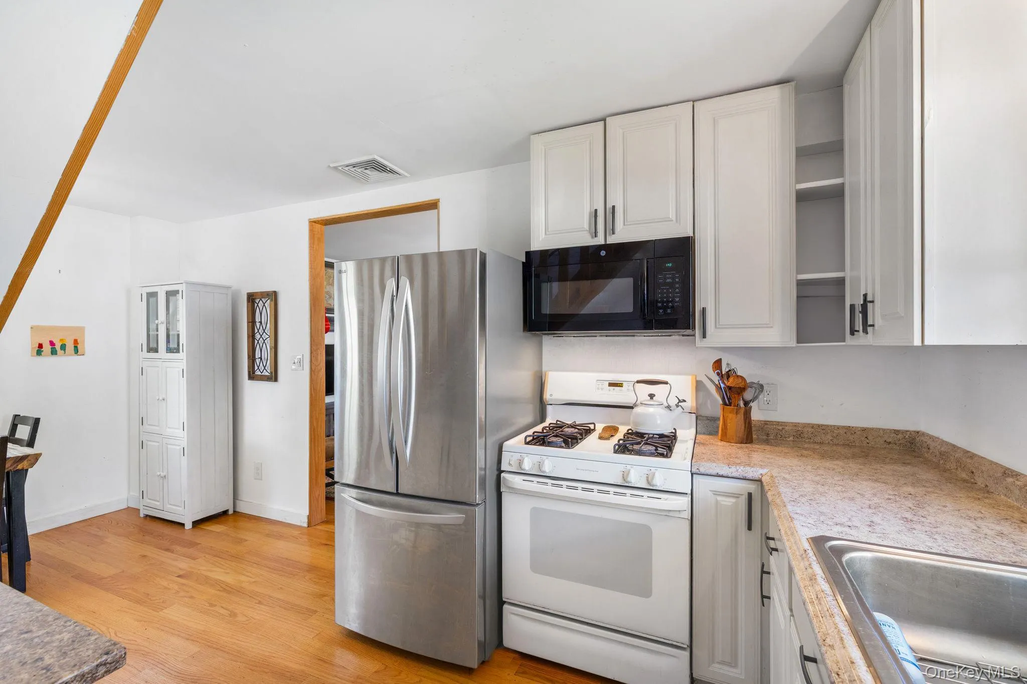 Kitchen featuring wood-finish flooring, white cabinetry with dark hardware, stainless steel refrigerator, white gas range, and a built-in microwave Kitchen featuring wood-finish flooring, white cabinetry with dark hardware, stainless steel refrigerator, white gas range, and a built-in microwave