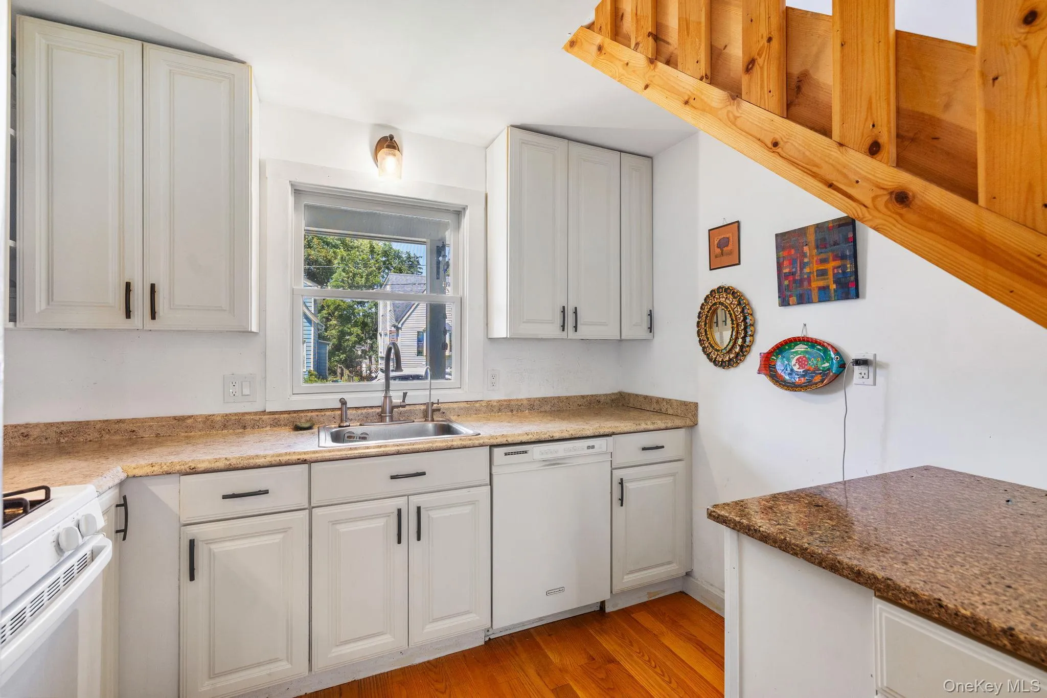 Kitchen featuring white cabinetry, light-colored countertops, hardwood flooring, and a stainless steel sink with a single-handle faucet Kitchen featuring white cabinetry, light-colored countertops, hardwood flooring, and a stainless steel sink with a single-handle faucet
