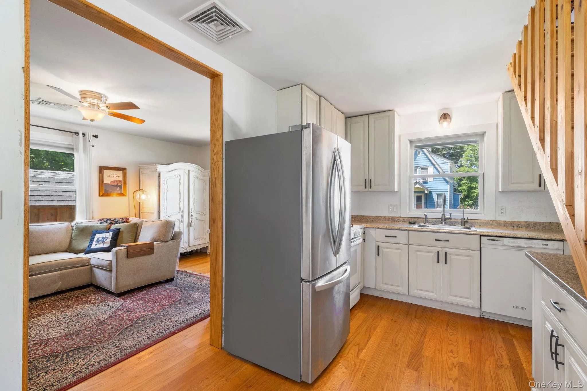 Kitchen featuring wood-finish flooring, white cabinetry, integrated stainless steel refrigerator, and a stainless steel sink with a window above Kitchen featuring wood-finish flooring, white cabinetry, integrated stainless steel refrigerator, and a stainless steel sink with a window above