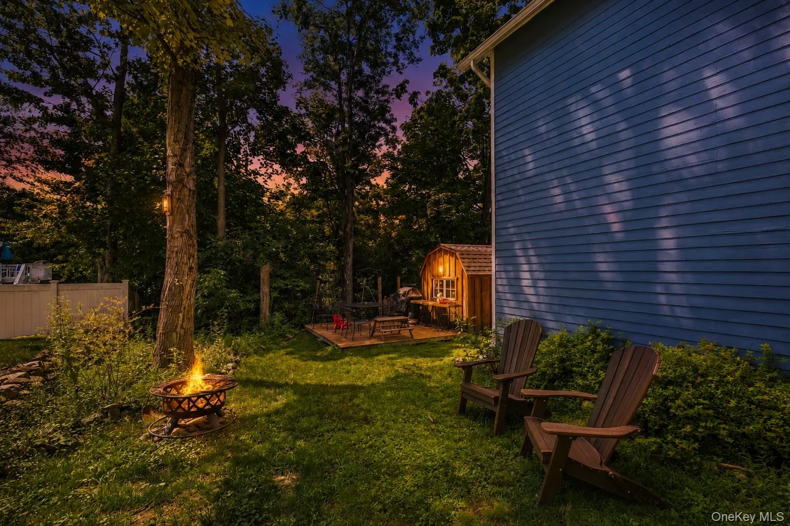 Grassed yard featuring a fire pit, mature trees, wood-sided shed, and a wooden deck Grassed yard featuring a fire pit, mature trees, wood-sided shed, and a wooden deck