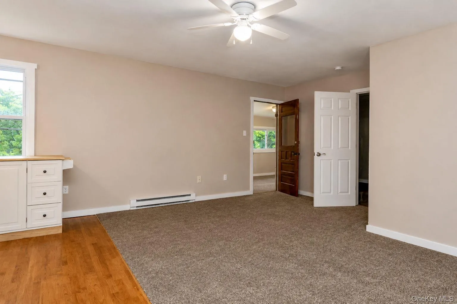 Spacious room featuring partial wood-finish flooring, neutral-toned carpeting, and a built-in white cabinet with three drawers Spacious room featuring partial wood-finish flooring, neutral-toned carpeting, and a built-in white cabinet with three drawers