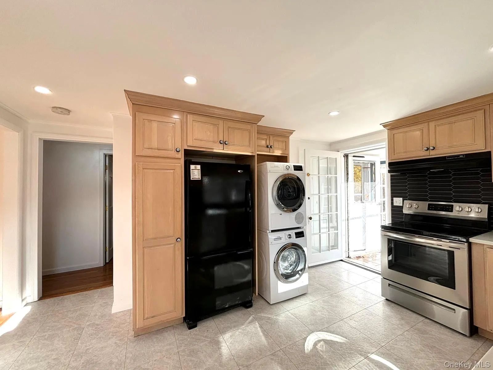 Kitchen with black refrigerator, backsplash, stainless steel range with electric stovetop, light tile patterned floors, and stacked washer / drying machine Kitchen with black refrigerator, backsplash, stainless steel range with electric stovetop, light tile patterned floors, and stacked washer / drying machine
