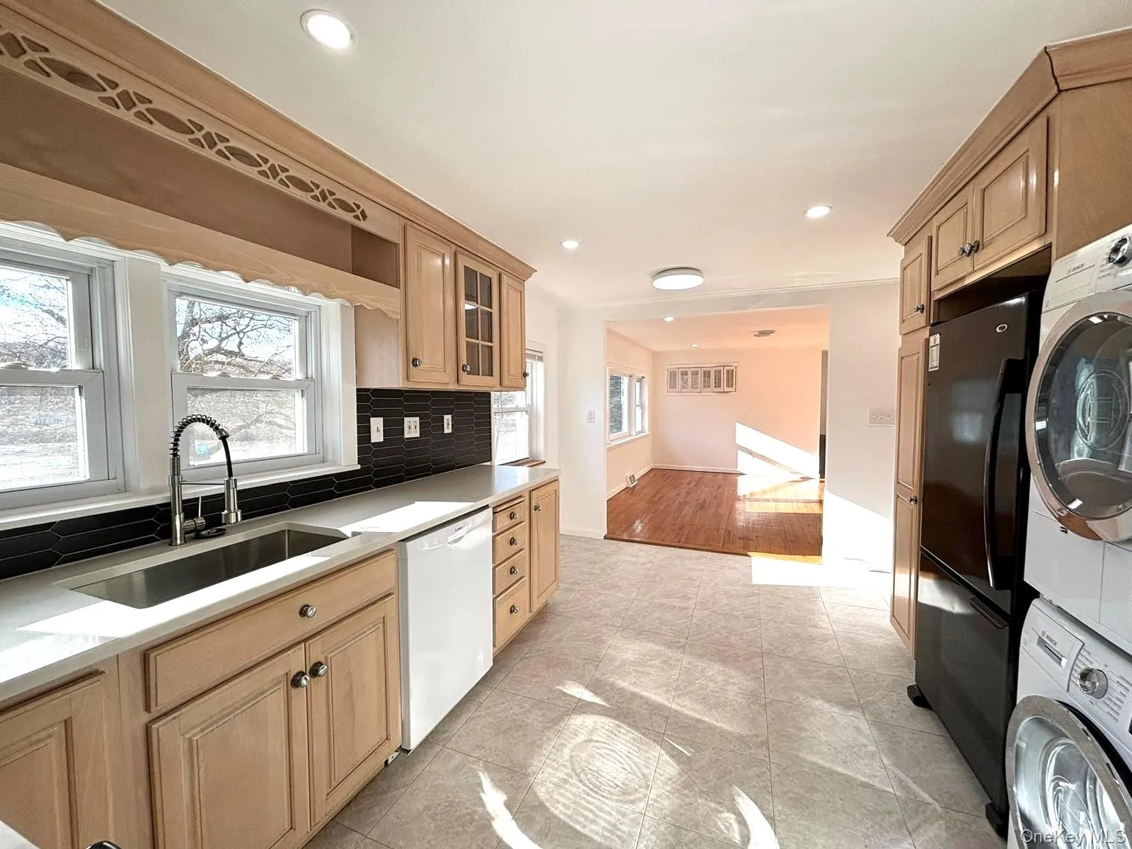 Kitchen featuring decorative backsplash, light hardwood / wood-style floors, white dishwasher, sink, and stacked washer and dryer Kitchen featuring decorative backsplash, light hardwood / wood-style floors, white dishwasher, sink, and stacked washer and dryer