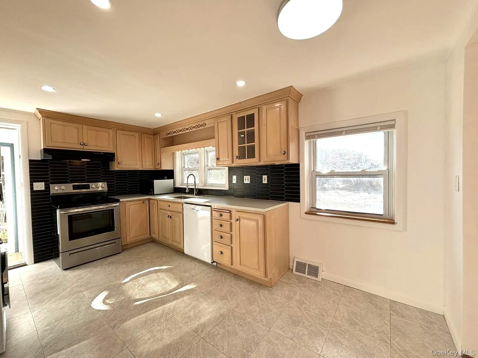 Kitchen with a wealth of natural light, light brown cabinets, white dishwasher, and stainless steel electric range Kitchen with a wealth of natural light, light brown cabinets, white dishwasher, and stainless steel electric range