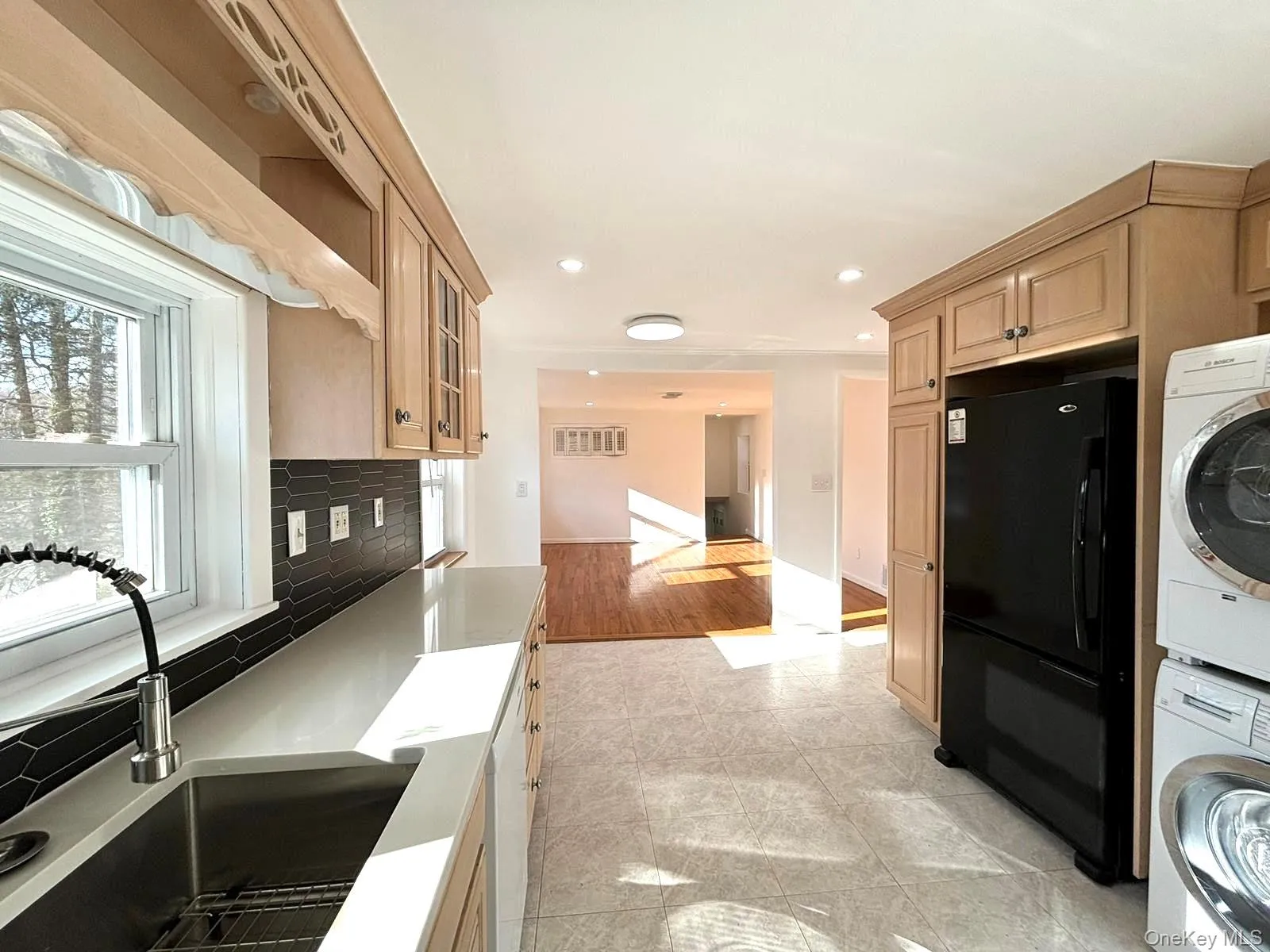 Kitchen featuring backsplash, black fridge, sink, light hardwood / wood-style flooring, and stacked washer and clothes dryer Kitchen featuring backsplash, black fridge, sink, light hardwood / wood-style flooring, and stacked washer and clothes dryer