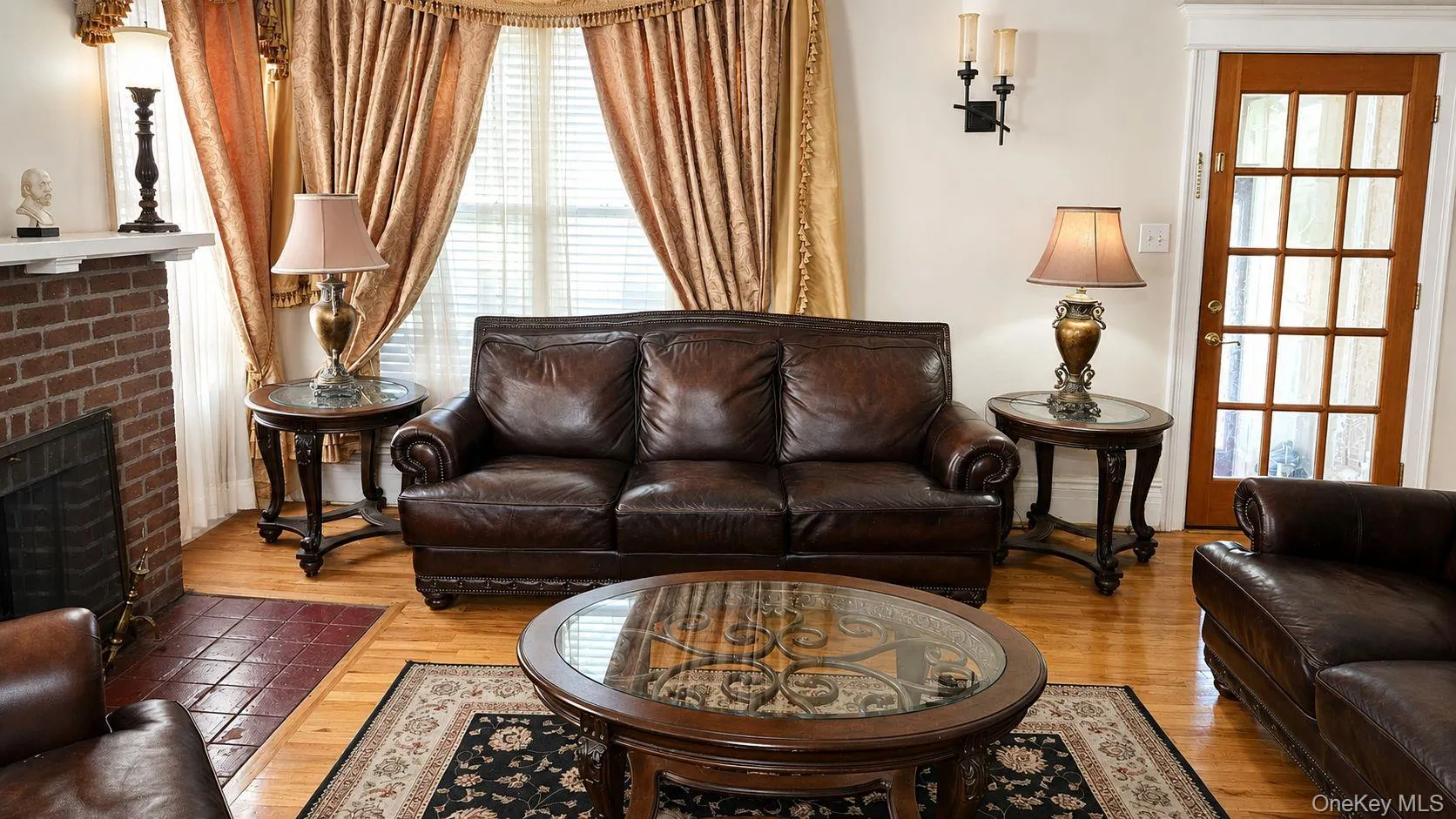 Living area featuring wood-finish flooring, a brick fireplace with a white mantel, and a multi-pane wood-finish door Living area featuring wood-finish flooring, a brick fireplace with a white mantel, and a multi-pane wood-finish door