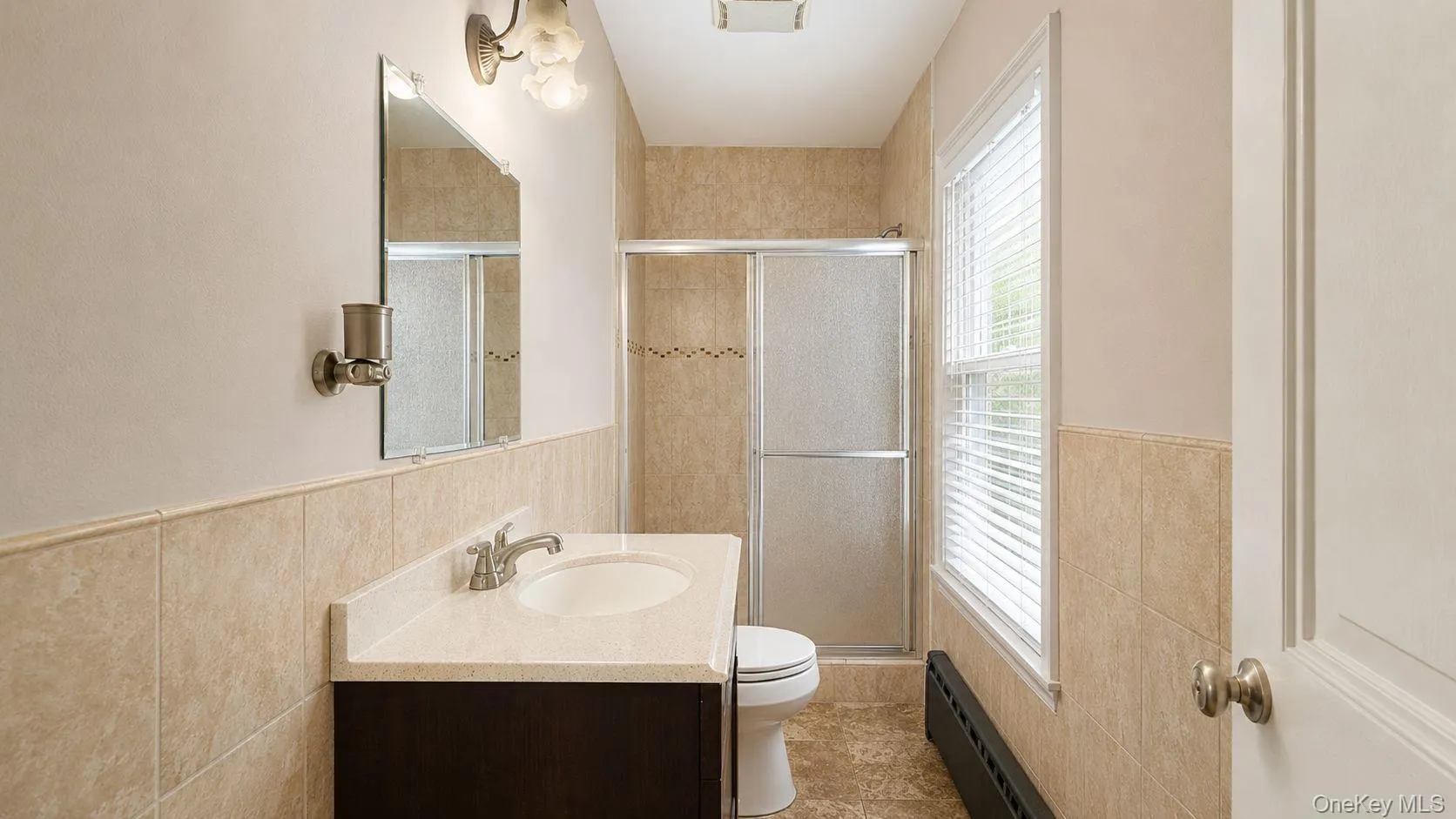 Bathroom featuring a dark wood-finish vanity with an integrated sink and brushed nickel faucet, a frameless mirror, and a tiled shower with a sliding glass door Bathroom featuring a dark wood-finish vanity with an integrated sink and brushed nickel faucet, a frameless mirror, and a tiled shower with a sliding glass door
