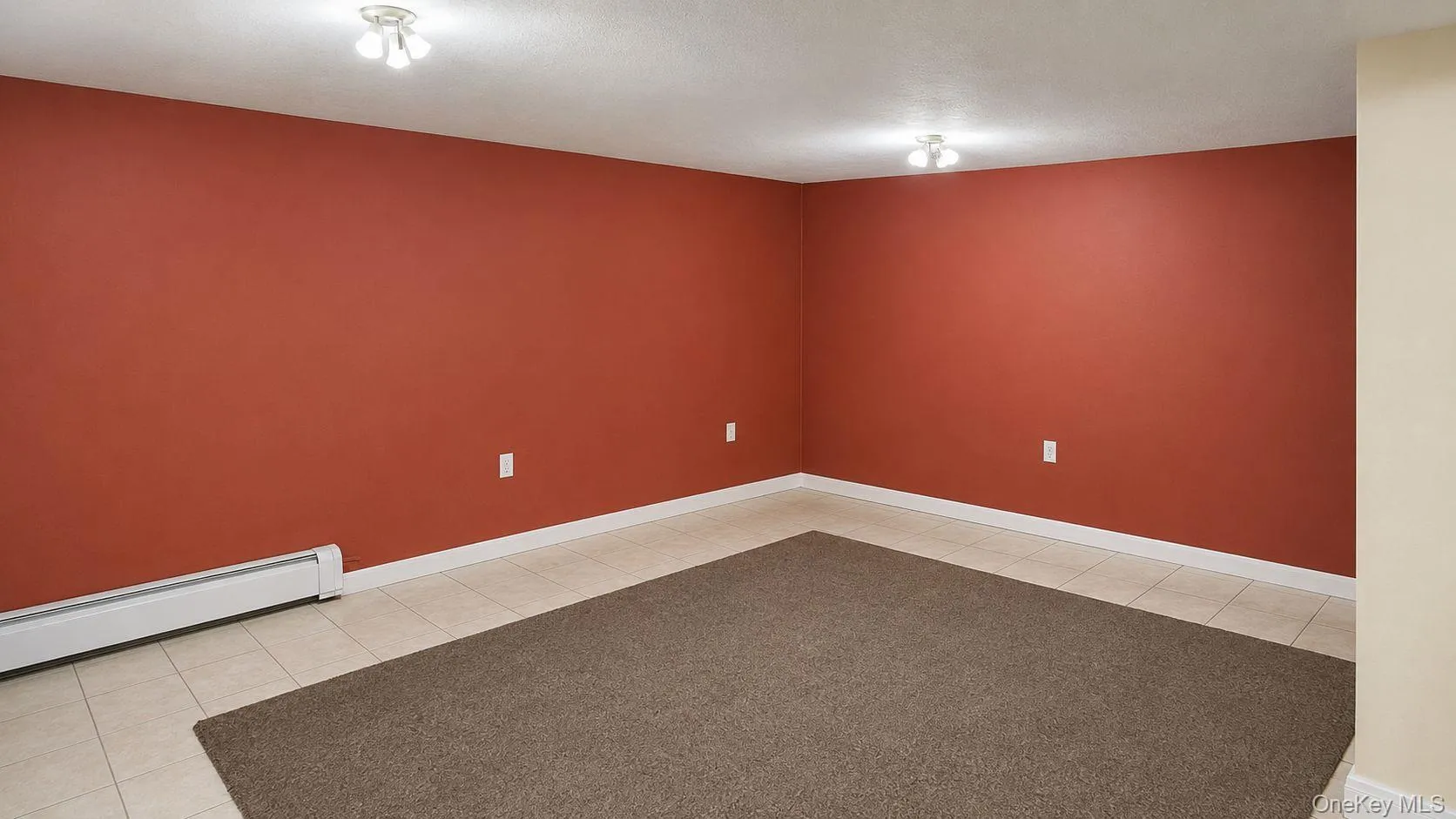 Spacious room with terra cotta walls, light-colored tile flooring, and overhead flush mount lighting Spacious room with terra cotta walls, light-colored tile flooring, and overhead flush mount lighting