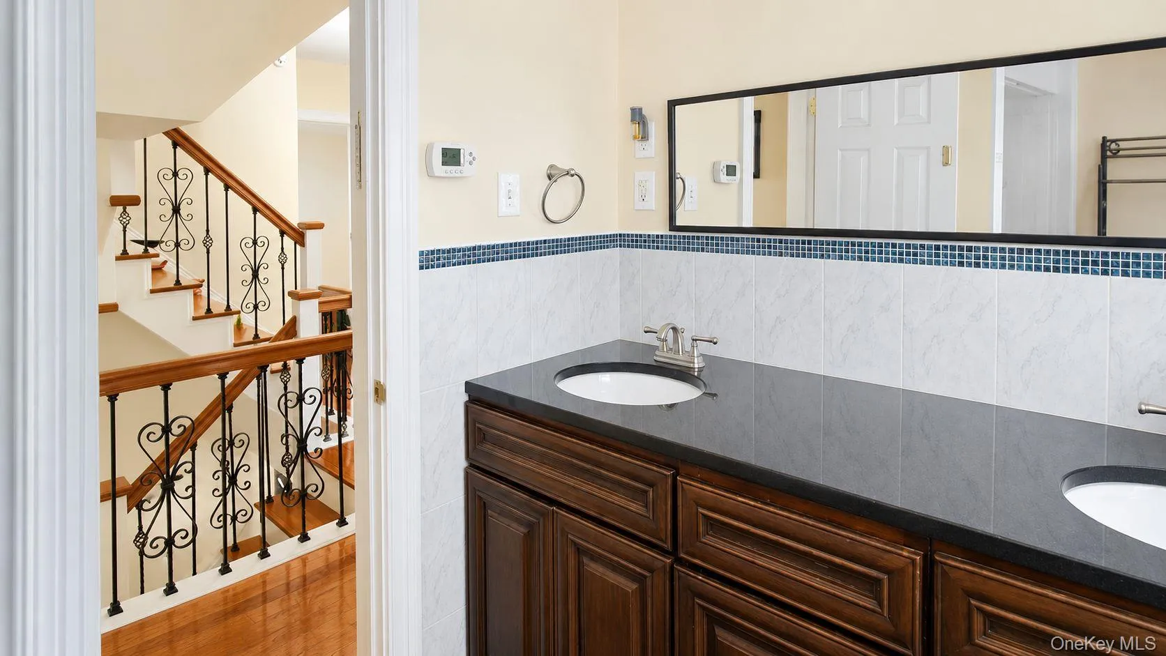 Dual-sink vanity with a dark wood-finish cabinet, dark countertop, and white under-mount sinks Dual-sink vanity with a dark wood-finish cabinet, dark countertop, and white under-mount sinks