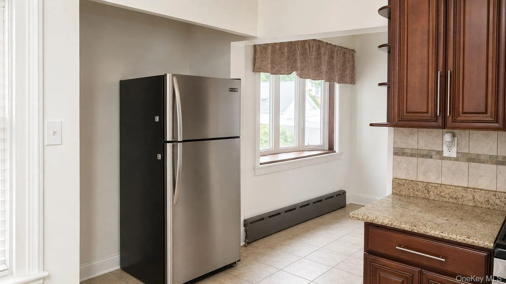 Kitchen area featuring warm wood cabinetry, neutral tile flooring, and a window providing natural light Kitchen area featuring warm wood cabinetry, neutral tile flooring, and a window providing natural light