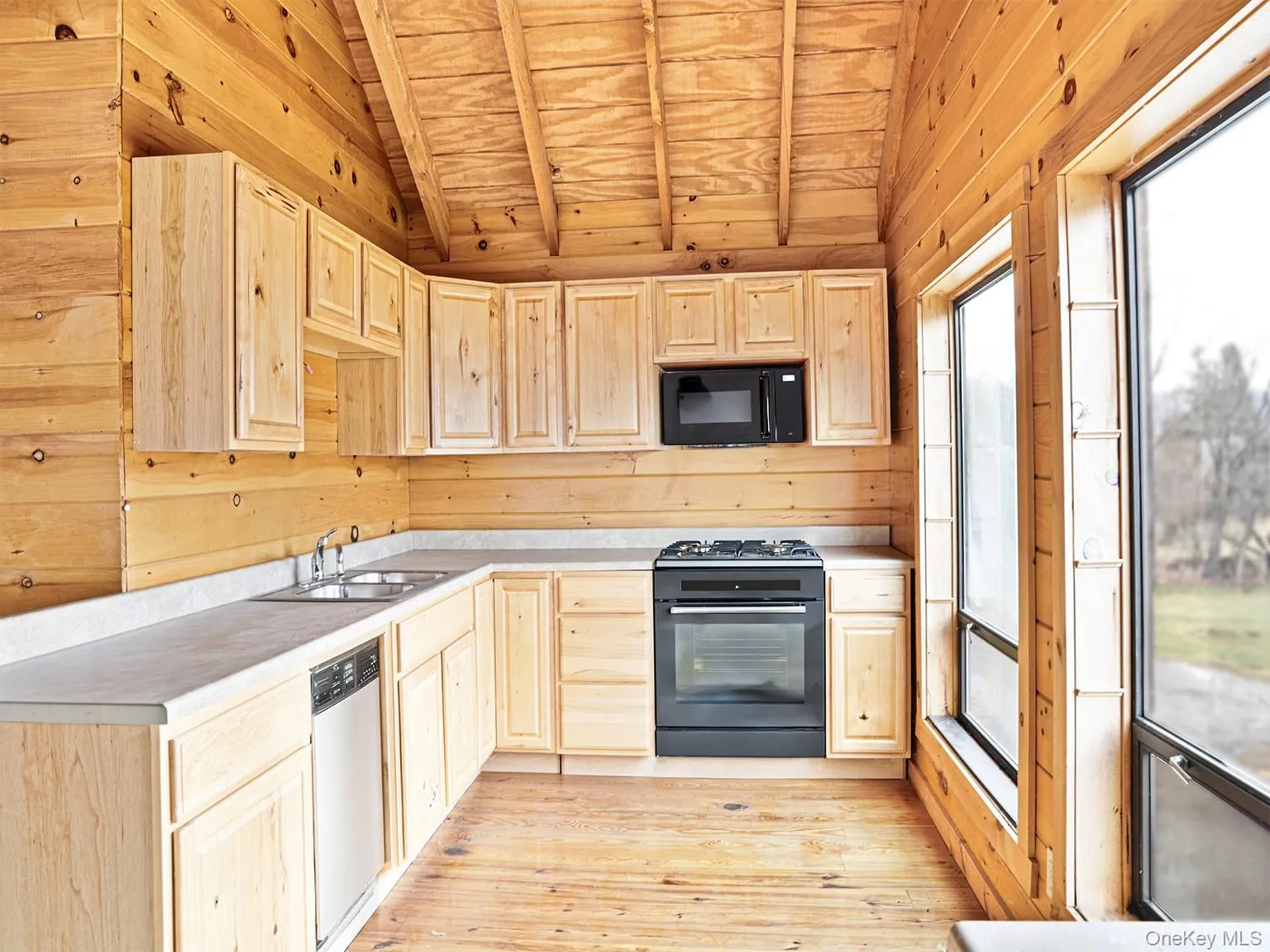 Kitchen featuring light brown cabinetry, black appliances, lofted ceiling, wooden ceiling, and wooden walls Kitchen featuring light brown cabinetry, black appliances, lofted ceiling, wooden ceiling, and wooden walls