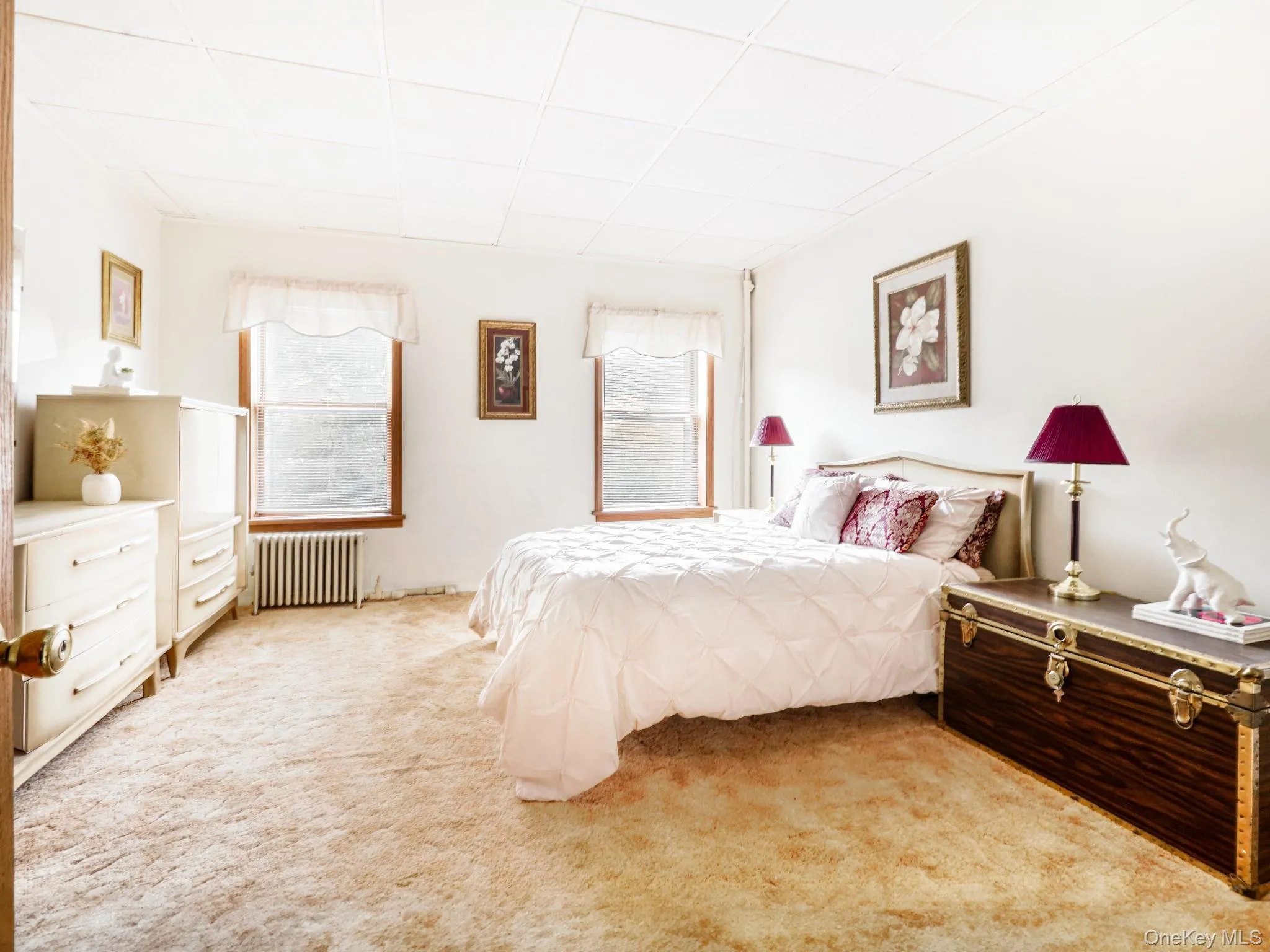Bedroom with radiator heating unit, light carpet, and a paneled ceiling Bedroom with radiator heating unit, light carpet, and a paneled ceiling