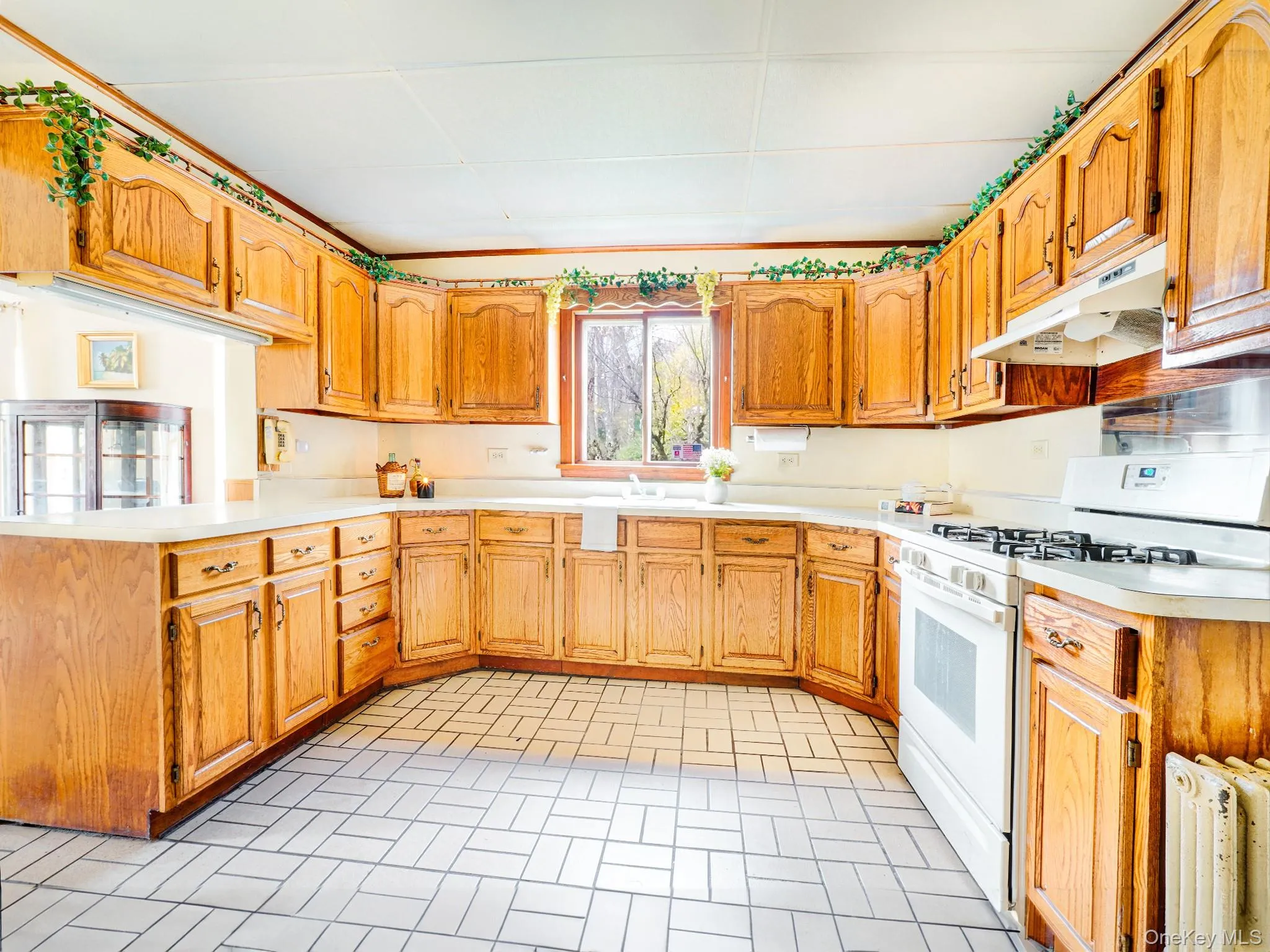 Kitchen with white gas range, under cabinet range hood, light countertops, brick patterned floors, and a sink Kitchen with white gas range, under cabinet range hood, light countertops, brick patterned floors, and a sink