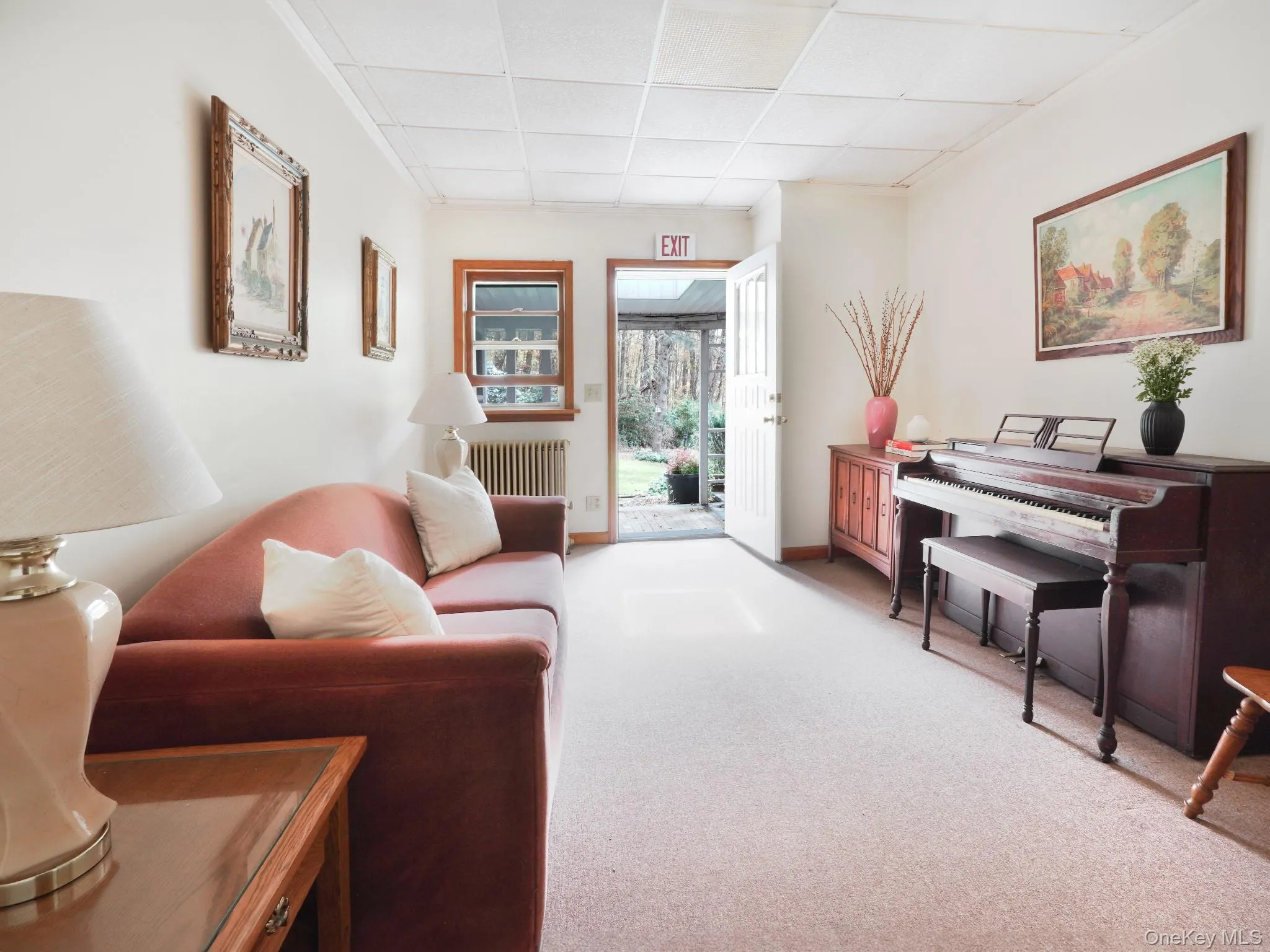 Living room with radiator heating unit, light carpet, baseboards, and a paneled ceiling Living room with radiator heating unit, light carpet, baseboards, and a paneled ceiling