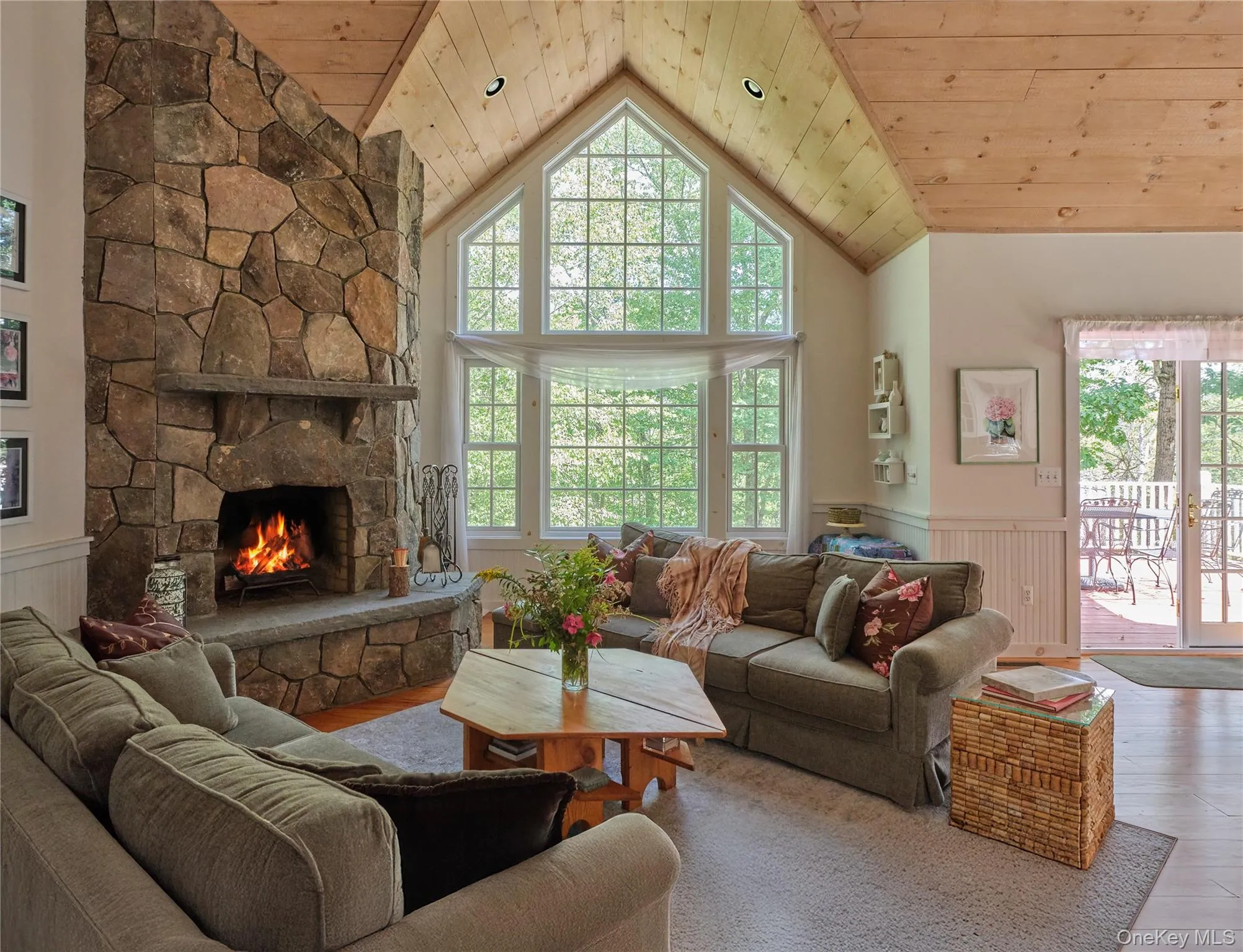 Living room with wainscoting, wood ceiling, a stone fireplace, high vaulted ceiling, and wood finished floors Living room with wainscoting, wood ceiling, a stone fireplace, high vaulted ceiling, and wood finished floors