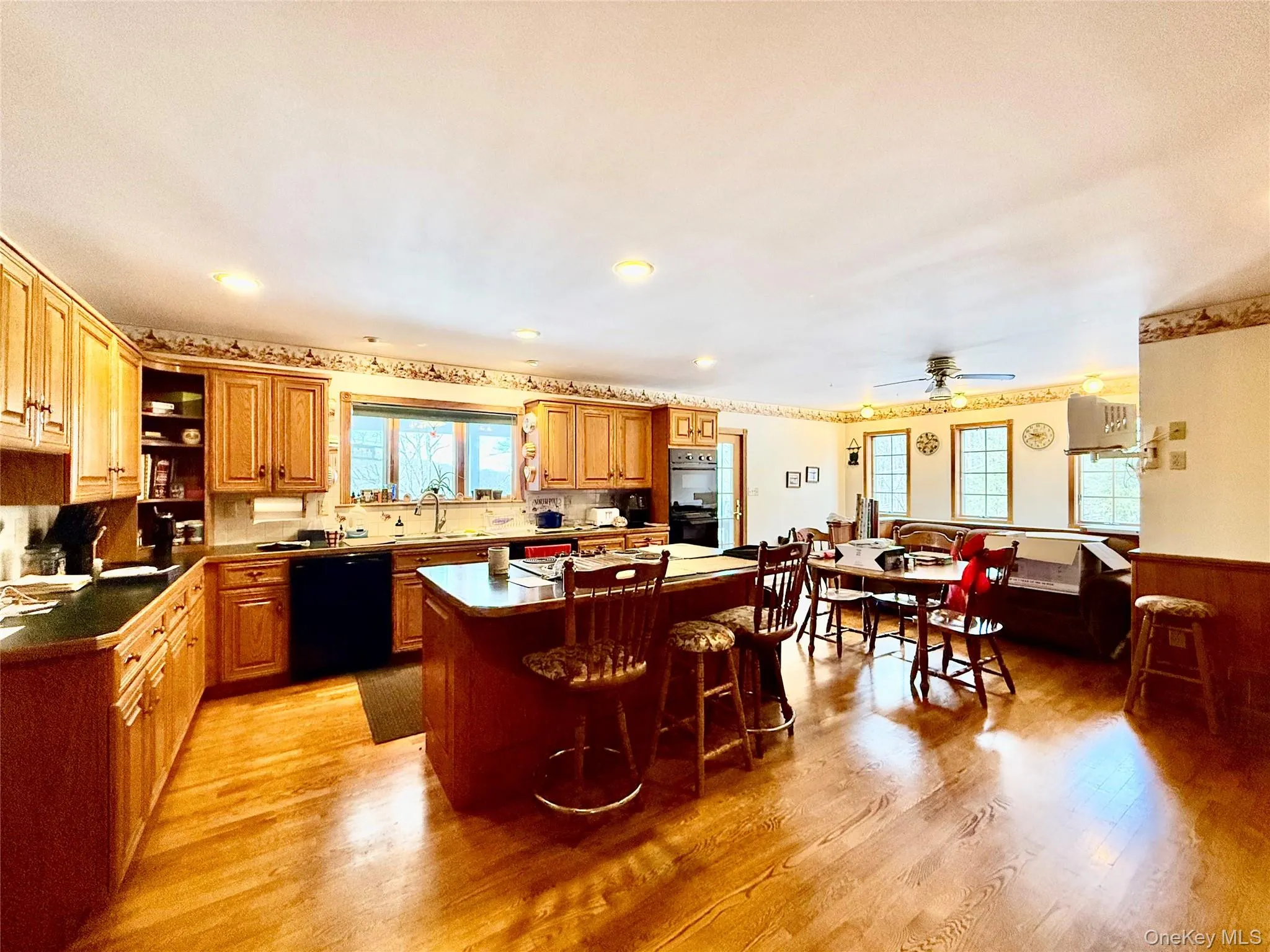 Kitchen with plenty of natural light, wood finish cabinetry, light wood-type flooring, dark countertops, and wainscoting Kitchen with plenty of natural light, wood finish cabinetry, light wood-type flooring, dark countertops, and wainscoting
