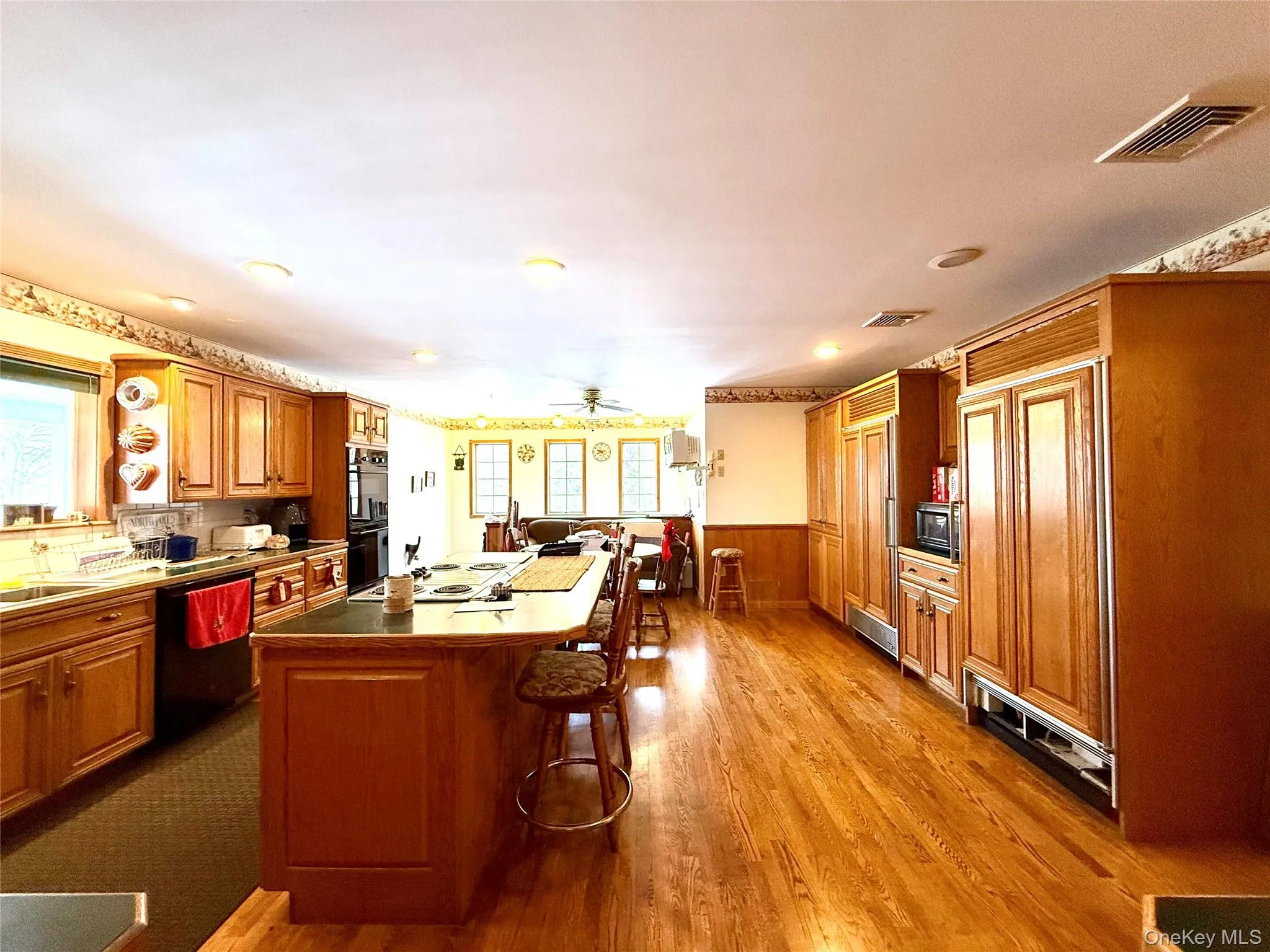 Kitchen with a kitchen breakfast bar, wood finish cabinets, black appliances, a kitchen island, and dark wood finished floors Kitchen with a kitchen breakfast bar, wood finish cabinets, black appliances, a kitchen island, and dark wood finished floors