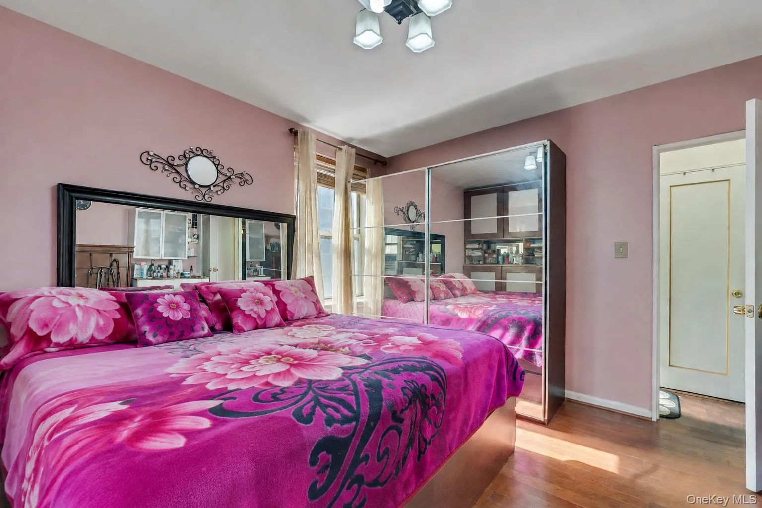 Bedroom featuring wood-finish flooring, a contemporary ceiling light fixture, a mirrored wardrobe, and a window with vertical blinds Bedroom featuring wood-finish flooring, a contemporary ceiling light fixture, a mirrored wardrobe, and a window with vertical blinds