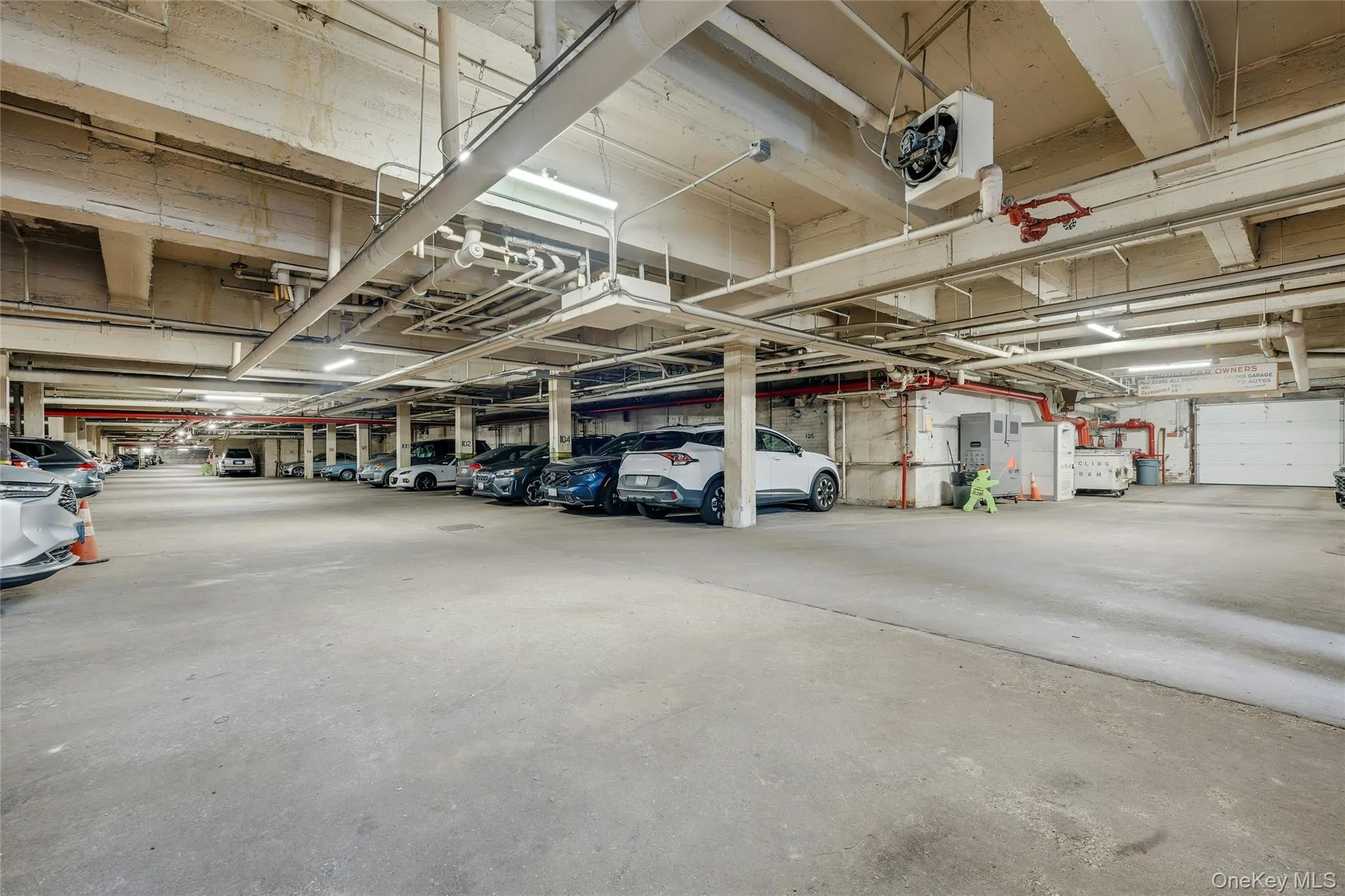 Spacious underground parking facility with concrete flooring, overhead lighting, visible utility conduits, and multiple designated parking stalls Spacious underground parking facility with concrete flooring, overhead lighting, visible utility conduits, and multiple designated parking stalls