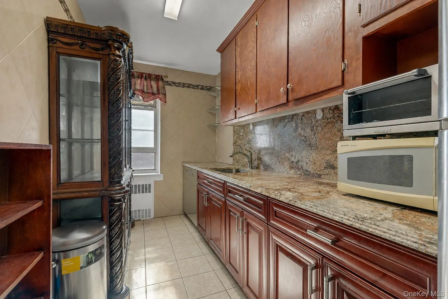 Galley kitchen featuring wood-finish cabinetry, stone countertops, and a coordinating stone backsplash Galley kitchen featuring wood-finish cabinetry, stone countertops, and a coordinating stone backsplash