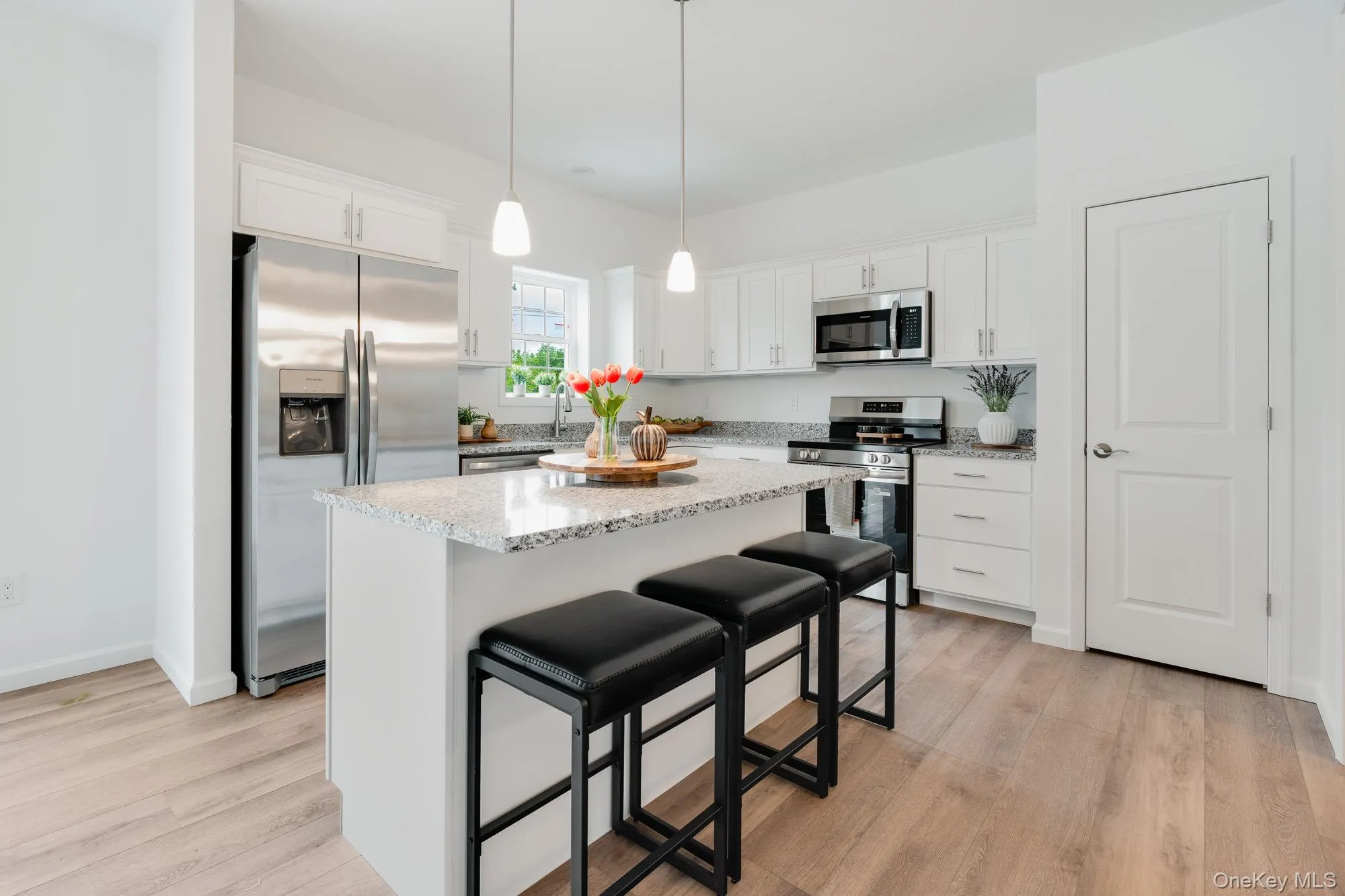 Kitchen with stainless steel appliances, white cabinets, a kitchen island, pantry and light wood-style flooring Kitchen with stainless steel appliances, white cabinets, a kitchen island, pantry and light wood-style flooring
