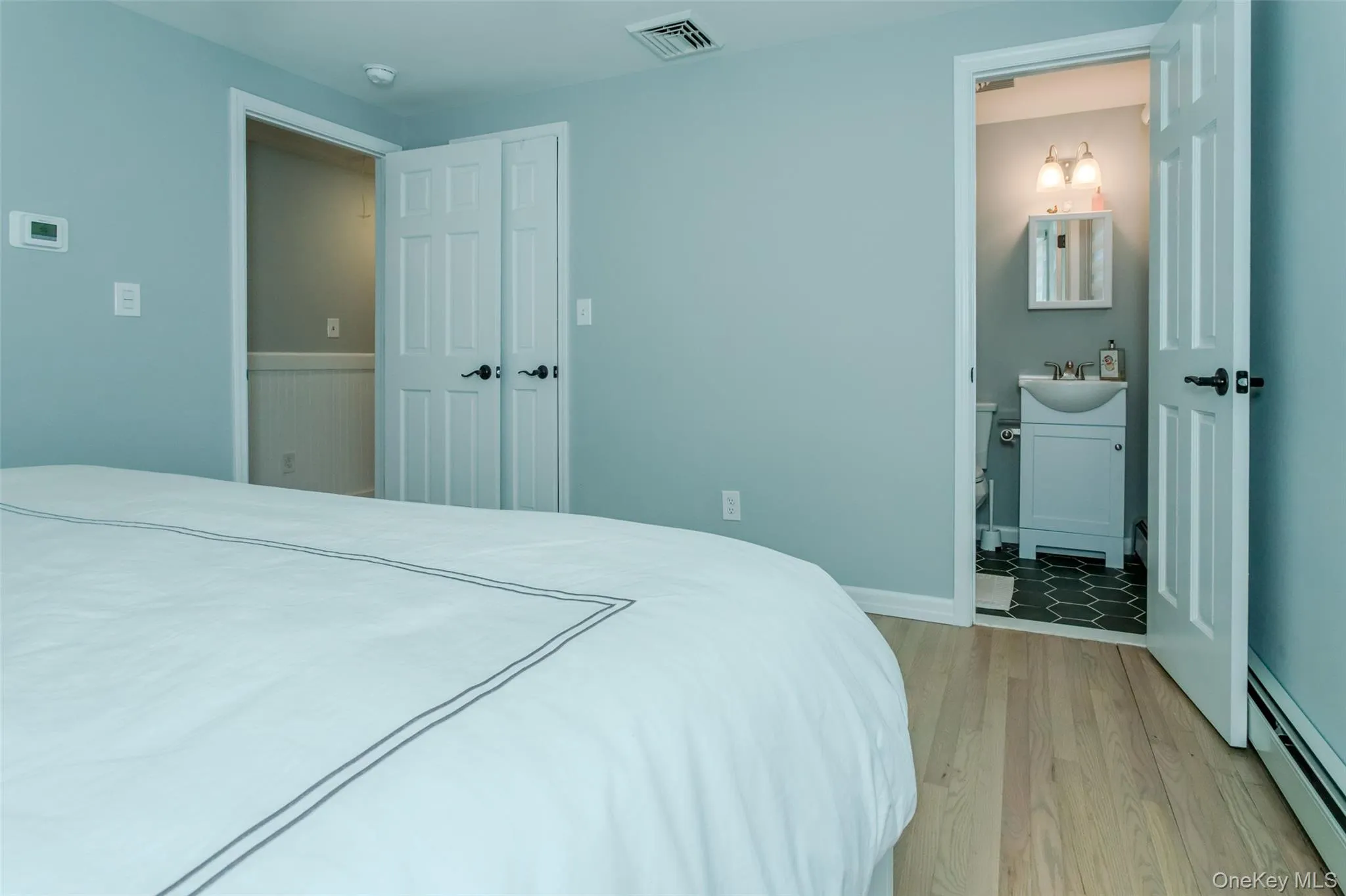 Bedroom featuring connected bathroom, light hardwood / wood-style floors, baseboard heating, and sink Bedroom featuring connected bathroom, light hardwood / wood-style floors, baseboard heating, and sink