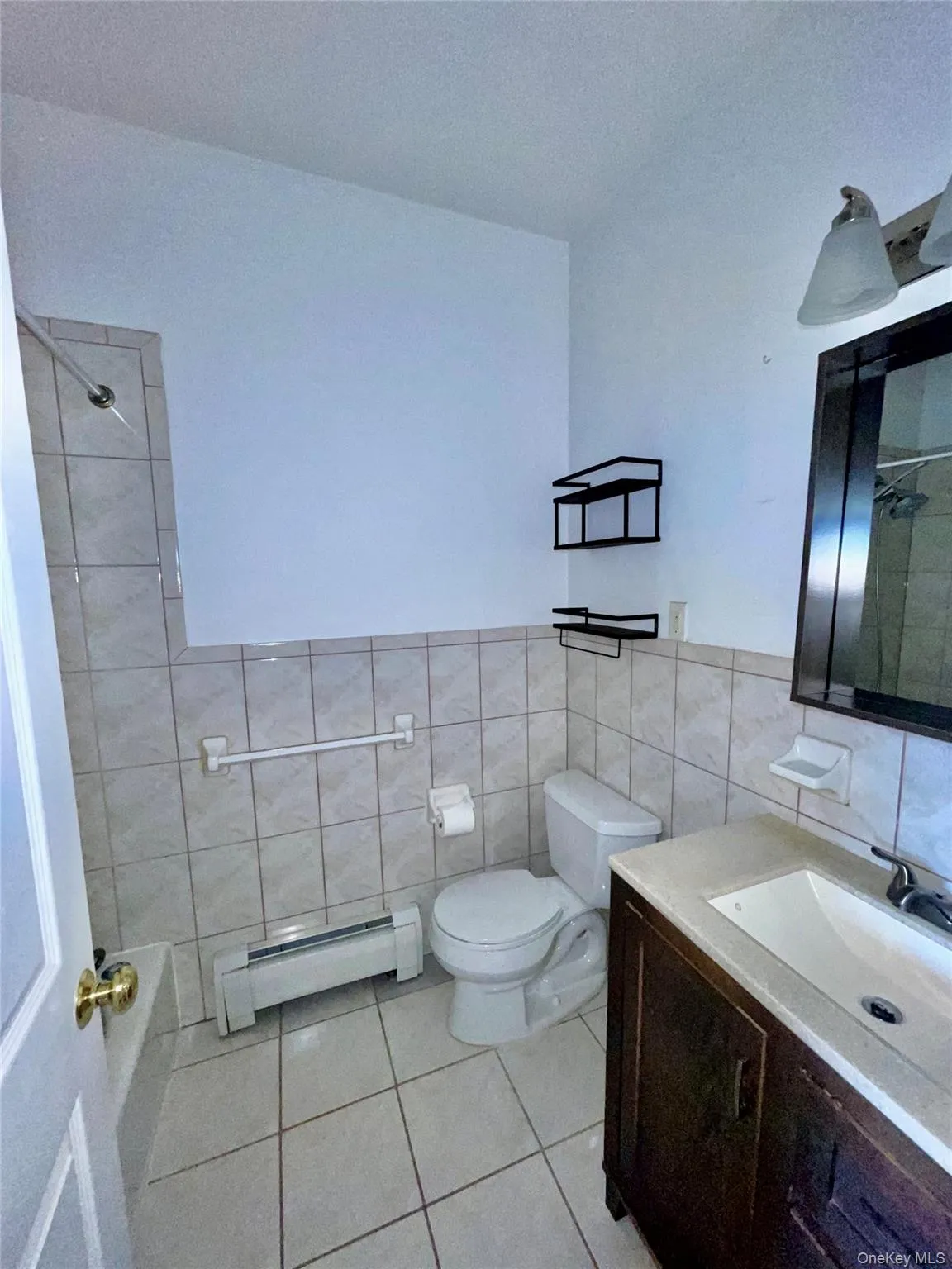 Bathroom featuring baseboard heating, tile walls, tile patterned floors, vanity, and bathing tub / shower combination Bathroom featuring baseboard heating, tile walls, tile patterned floors, vanity, and bathing tub / shower combination