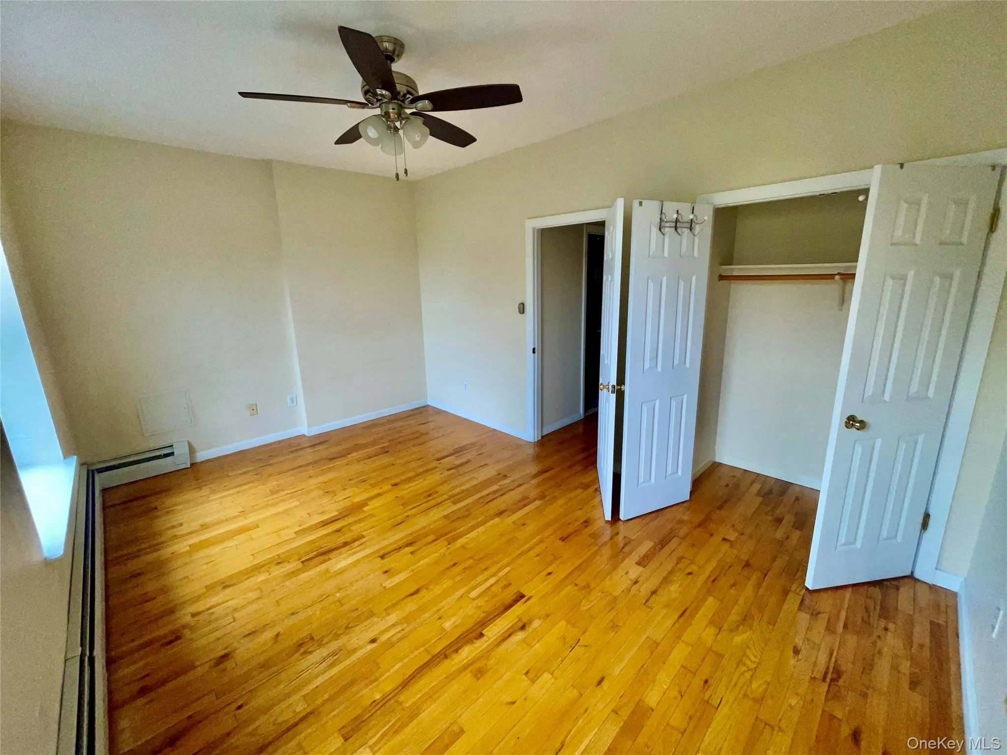 Unfurnished bedroom with light wood finished floors, a closet, ceiling fan, and a baseboard heating unit Unfurnished bedroom with light wood finished floors, a closet, ceiling fan, and a baseboard heating unit