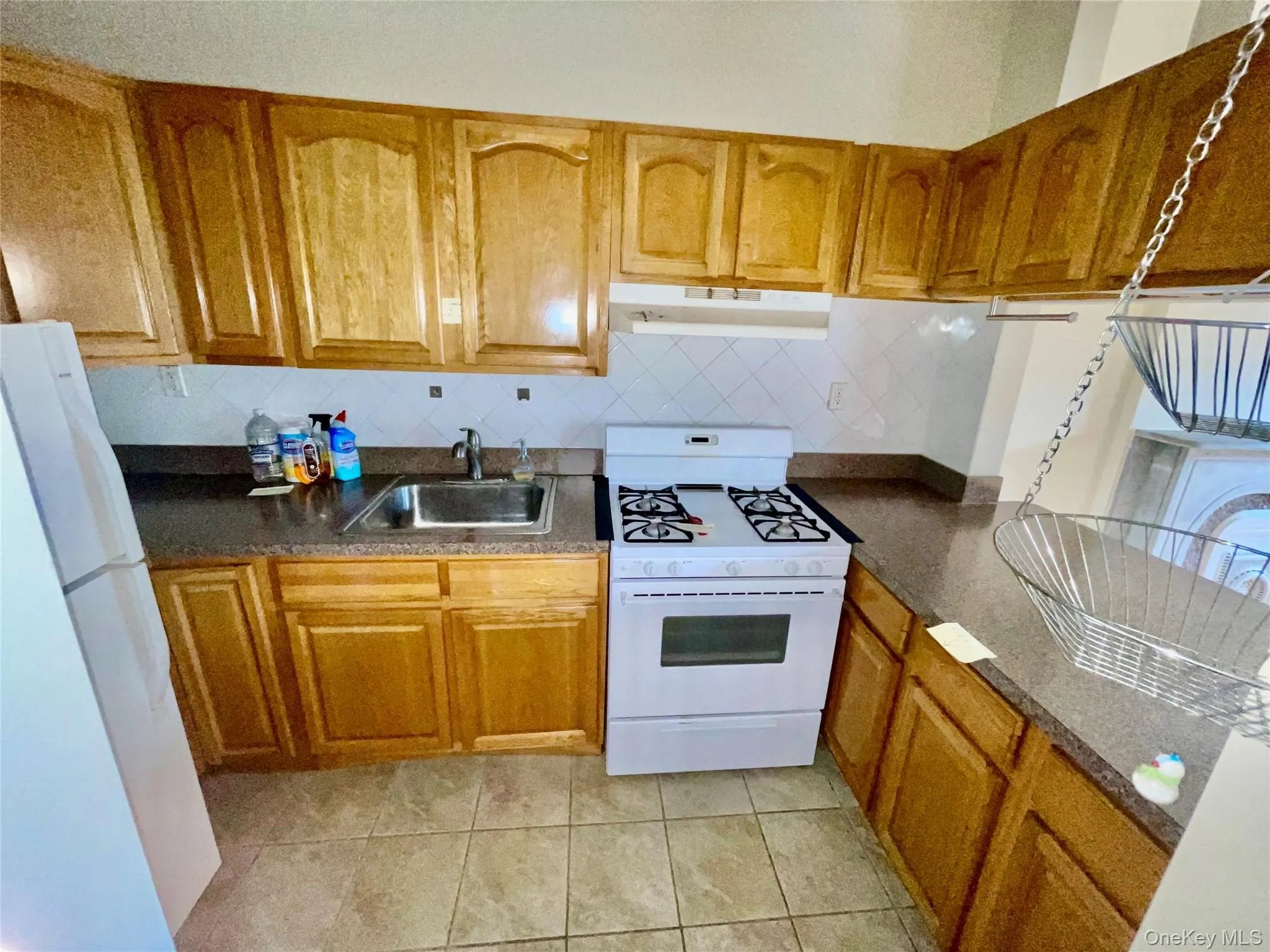 Kitchen featuring white appliances, brown cabinets, under cabinet range hood, and light tile patterned flooring Kitchen featuring white appliances, brown cabinets, under cabinet range hood, and light tile patterned flooring