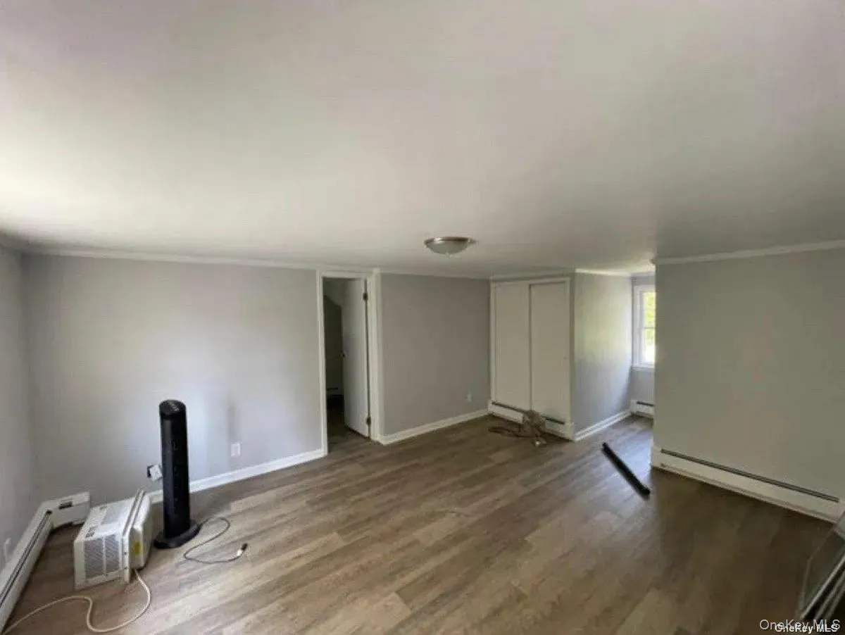 Unfurnished living room with a baseboard heating unit, baseboards, crown molding, and wood finished floors Unfurnished living room with a baseboard heating unit, baseboards, crown molding, and wood finished floors