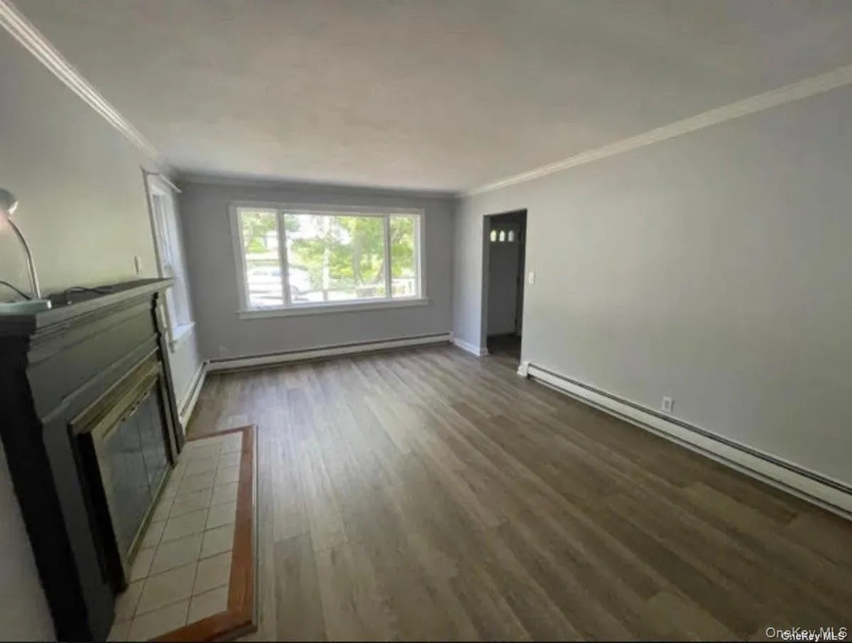 Unfurnished living room featuring baseboards, ornamental molding, baseboard heating, and wood finished floors Unfurnished living room featuring baseboards, ornamental molding, baseboard heating, and wood finished floors