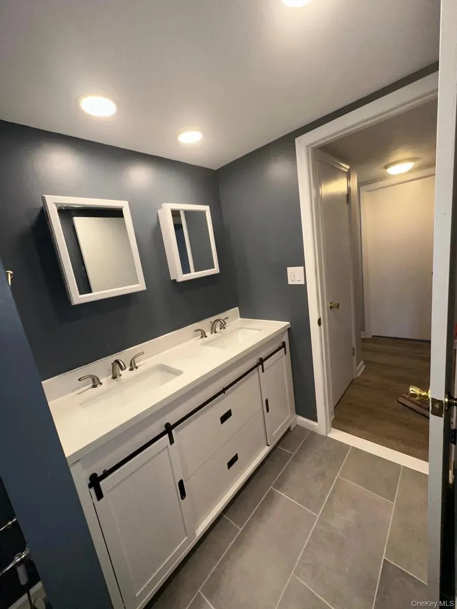 Bathroom featuring baseboards, tile patterned flooring, double vanity, and a sink Bathroom featuring baseboards, tile patterned flooring, double vanity, and a sink