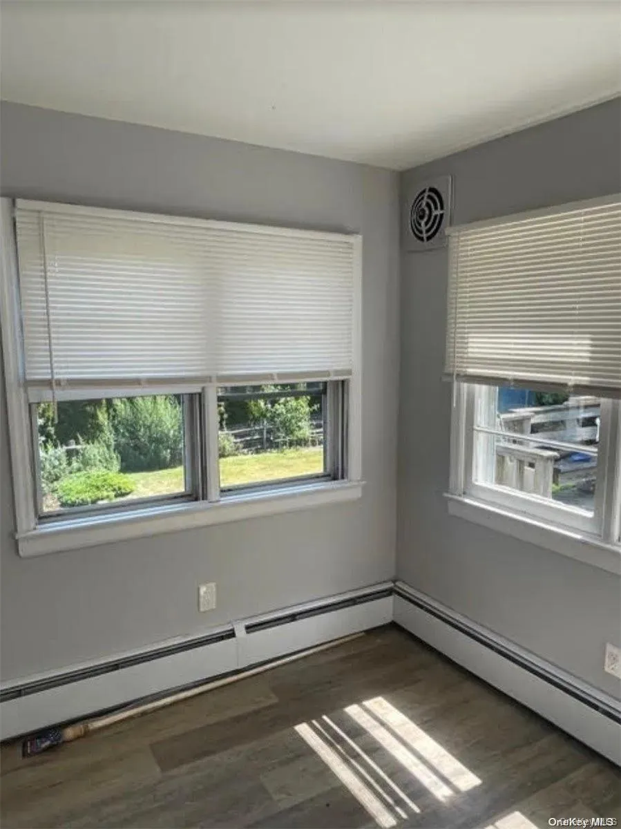 Empty room with a baseboard heating unit, visible vents, and wood finished floors Empty room with a baseboard heating unit, visible vents, and wood finished floors