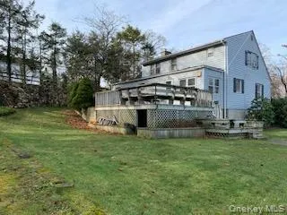 Back of property featuring a lawn, a deck, and a chimney Back of property featuring a lawn, a deck, and a chimney