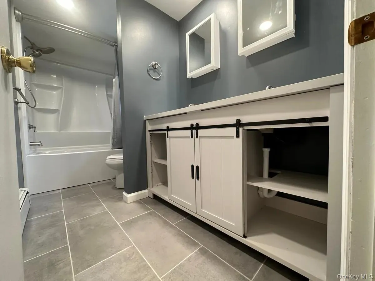 Full bath with toilet, shower / bath combo with shower curtain, vanity, tile patterned flooring, and baseboard heating Full bath with toilet, shower / bath combo with shower curtain, vanity, tile patterned flooring, and baseboard heating