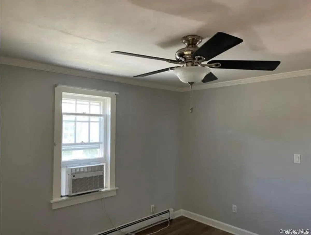 Empty room with crown molding, dark wood-style flooring, ceiling fan, baseboard heating, and baseboards Empty room with crown molding, dark wood-style flooring, ceiling fan, baseboard heating, and baseboards