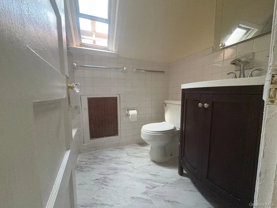 Spa-inspired primary bathroom featuring a walk-in shower with frameless glass enclosure and tile surround, dual vanity with dark wood cabinetry, marble-finish flooring, and abundant natural light from overhead window Spa-inspired primary bathroom featuring a walk-in shower with frameless glass enclosure and tile surround, dual vanity with dark wood cabinetry, marble-finish flooring, and abundant natural light from overhead window