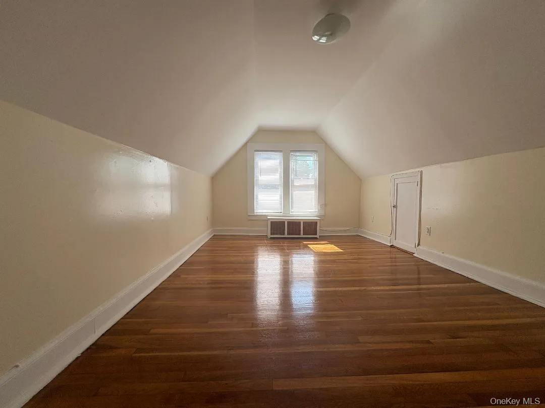 Bright attic room featuring soaring vaulted ceilings, rich wood-finish flooring throughout, and a dormer window allowing natural light Bright attic room featuring soaring vaulted ceilings, rich wood-finish flooring throughout, and a dormer window allowing natural light