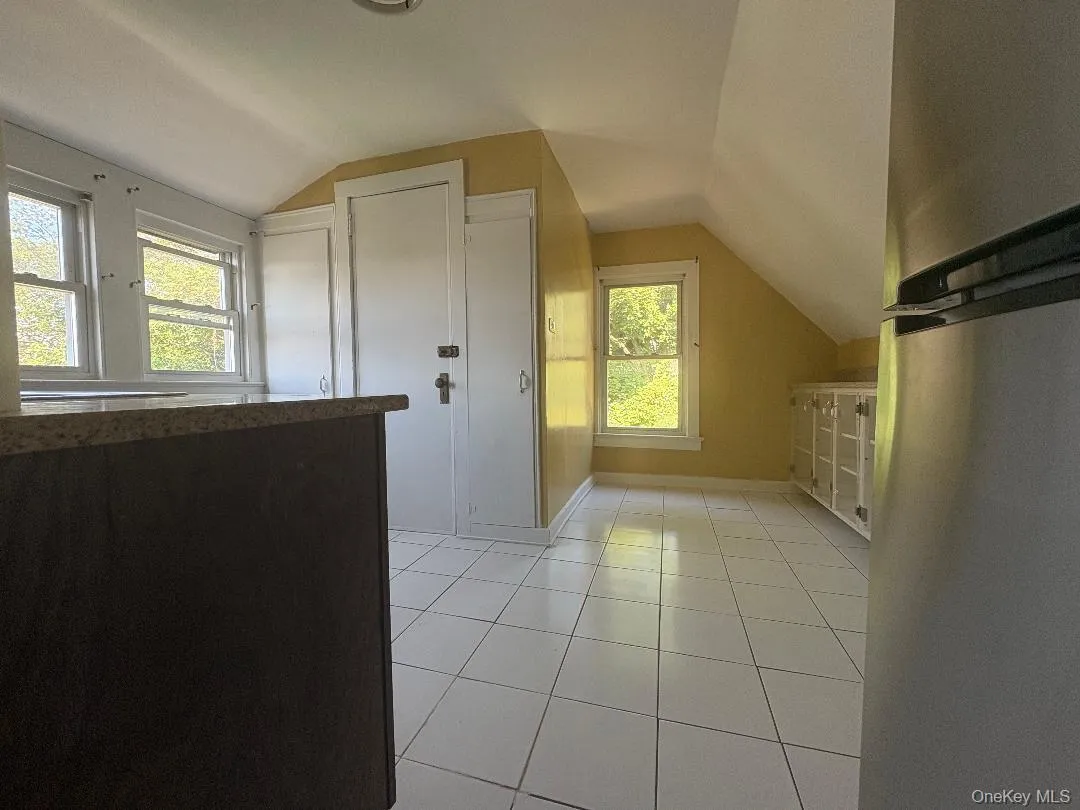 Bright upper-level room featuring sloped ceilings, multiple windows with natural light, ceramic tile flooring, and built-in cabinetry Bright upper-level room featuring sloped ceilings, multiple windows with natural light, ceramic tile flooring, and built-in cabinetry