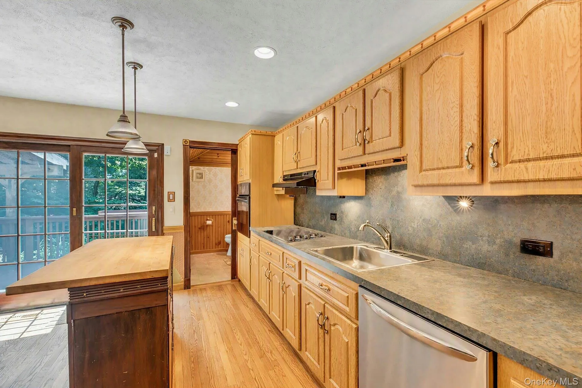 Kitchen featuring light wood cabinetry, a stainless steel dishwasher, a double basin sink, and pendant lighting Kitchen featuring light wood cabinetry, a stainless steel dishwasher, a double basin sink, and pendant lighting