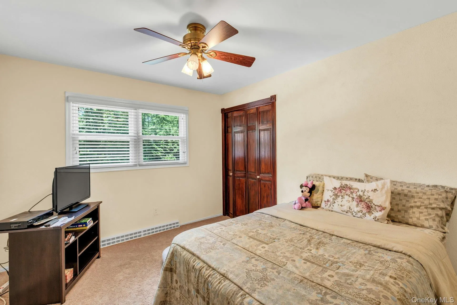 Bedroom featuring a ceiling fan with integrated lighting, a window with blinds, baseboard heating, and wood-paneled bifold closet doors Bedroom featuring a ceiling fan with integrated lighting, a window with blinds, baseboard heating, and wood-paneled bifold closet doors