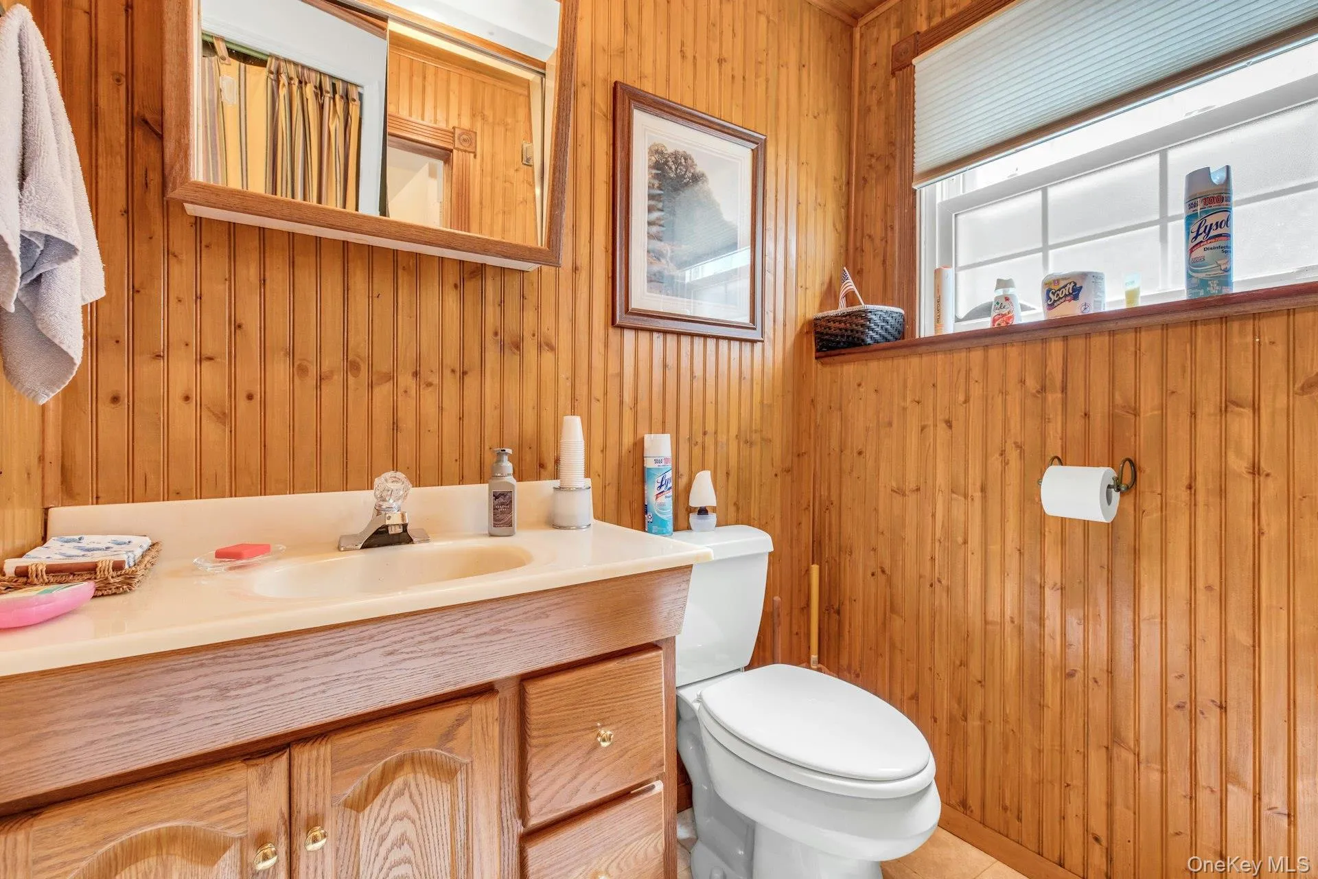 Warm wood-paneled bathroom featuring a wood-finish vanity with integrated sink, ceramic countertop, and ample storage cabinetry Warm wood-paneled bathroom featuring a wood-finish vanity with integrated sink, ceramic countertop, and ample storage cabinetry