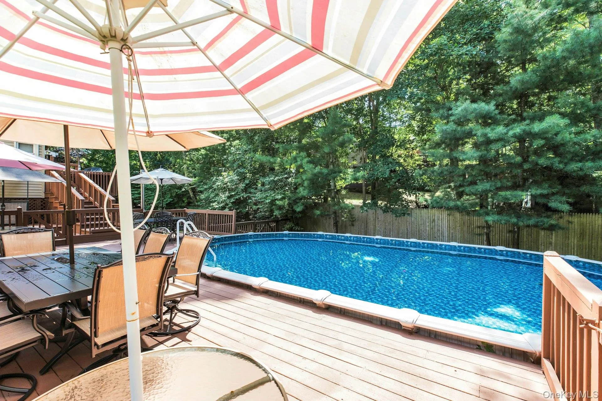 Expansive outdoor deck featuring an above-ground pool, wood fencing, and mature trees Expansive outdoor deck featuring an above-ground pool, wood fencing, and mature trees